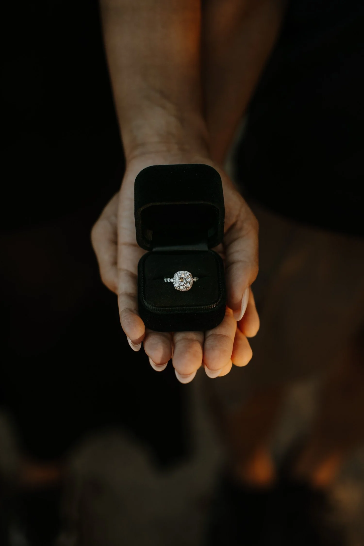 Close-up of an open ring box with a diamond engagement ring held in an outstretched hand
