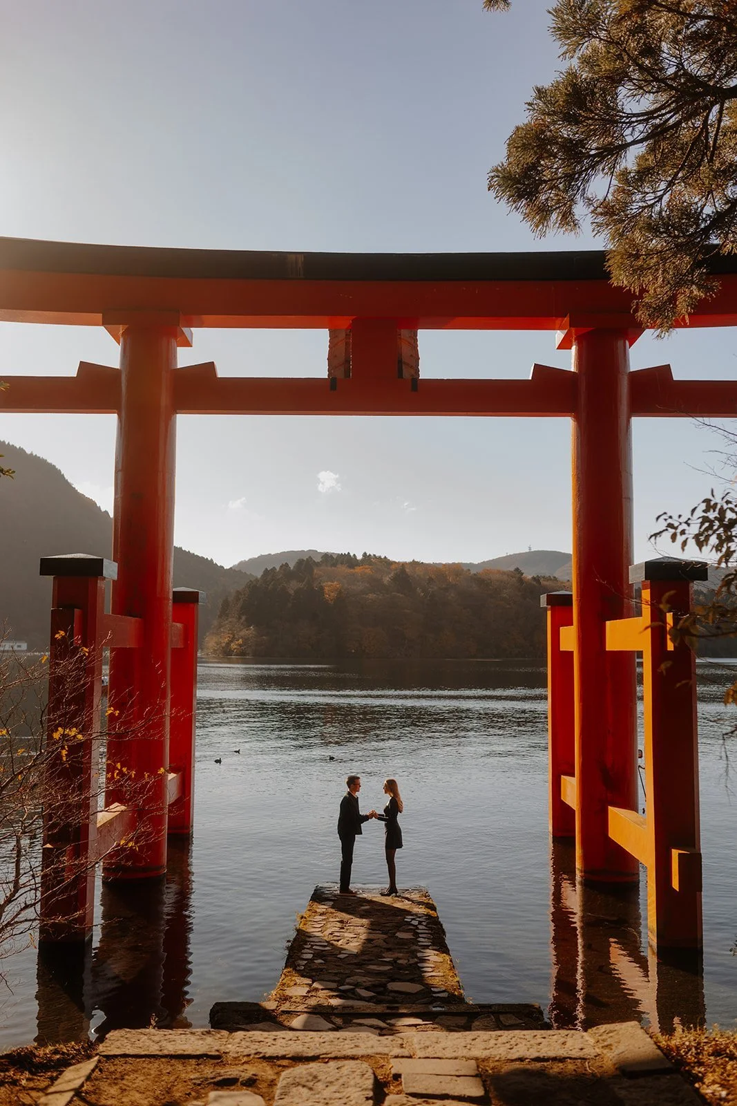 Newly engaged couple holding hands on the stone jetty beneath the torii gate, Lake Ashi, Hakone