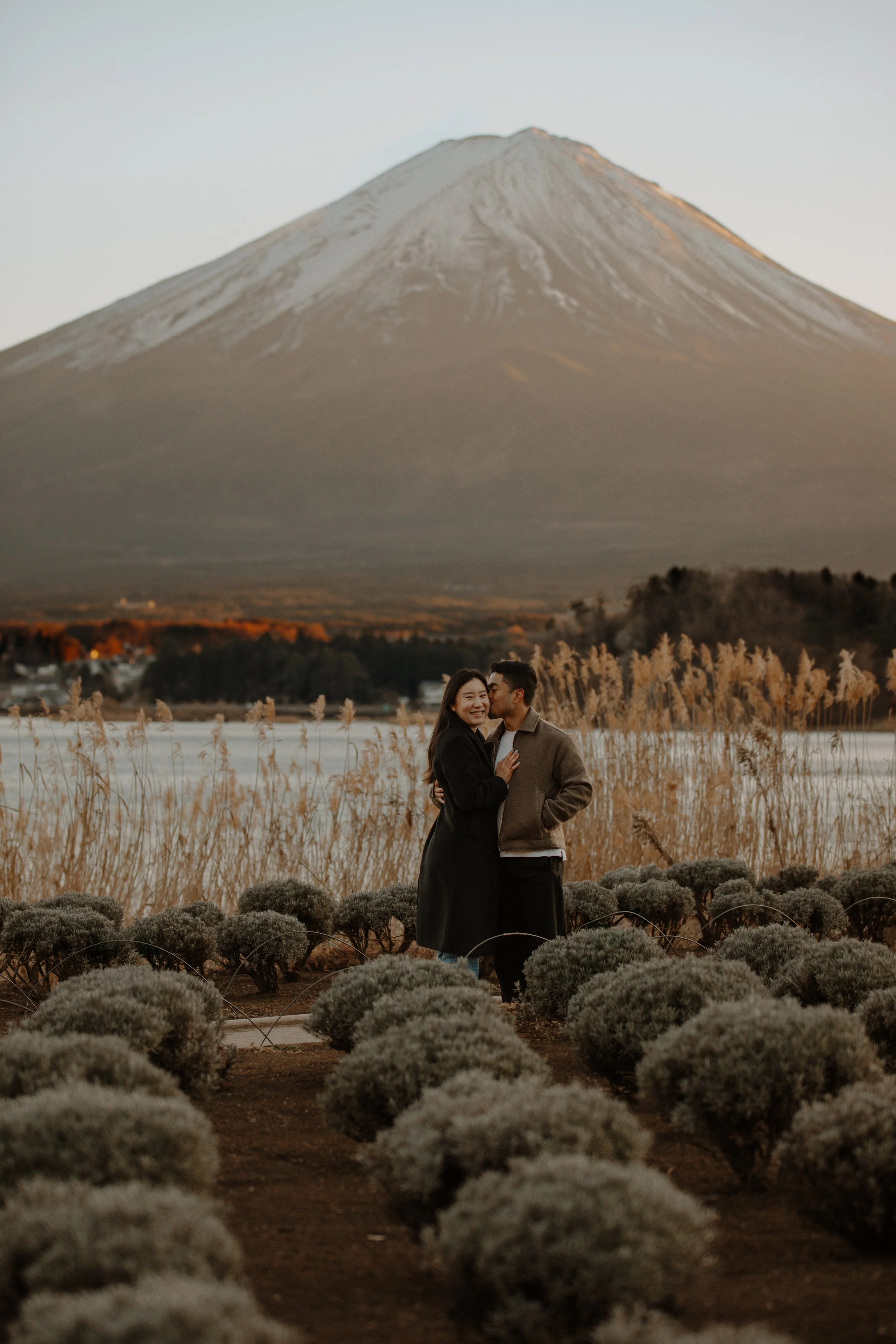 Couple embracing and laughing in a lavender field at sunset with Mount Fuji glowing behind them