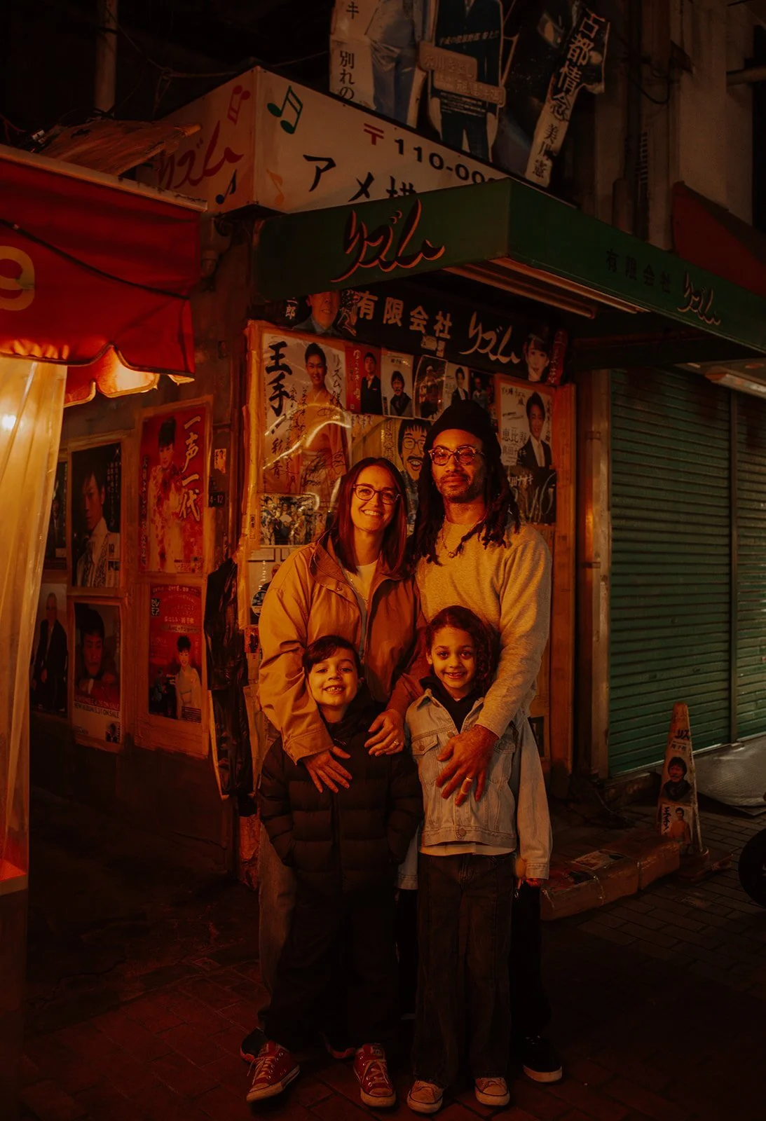 Family of four smiling together on a lantern-lit retro Tokyo shopping street during their family photography session.