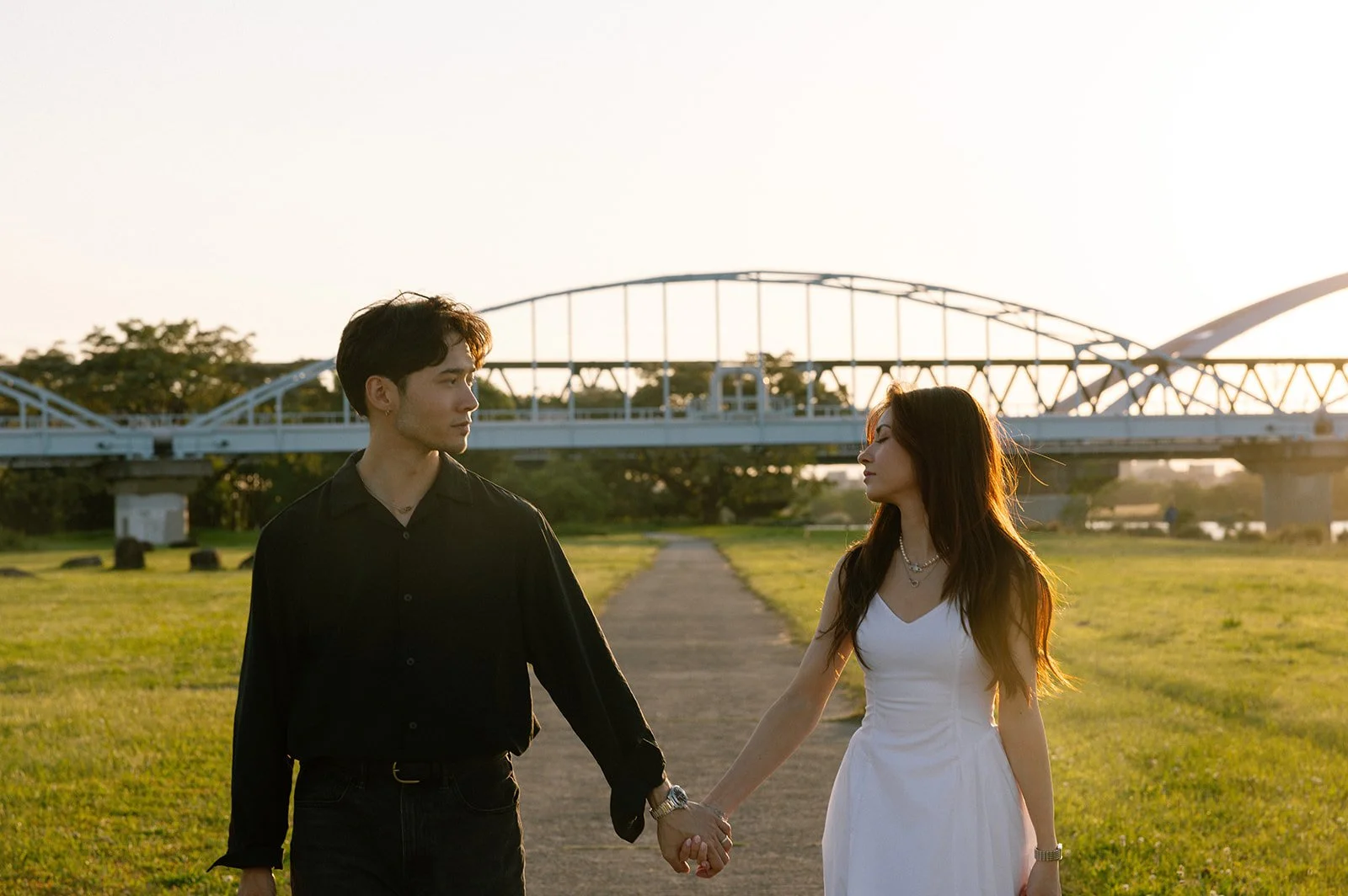 Vincent and Adriana holding hands in front of a steel arch bridge along the river in Osaka