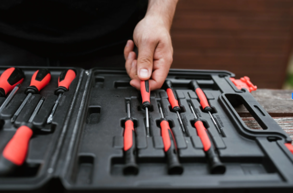 Person handling a set of screwdrivers in a black plastic toolbox with red handles.