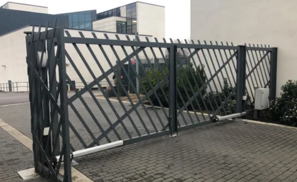 Black metal security gate with diagonal slats, installed in front of a building with a parking lot and some bushes.
