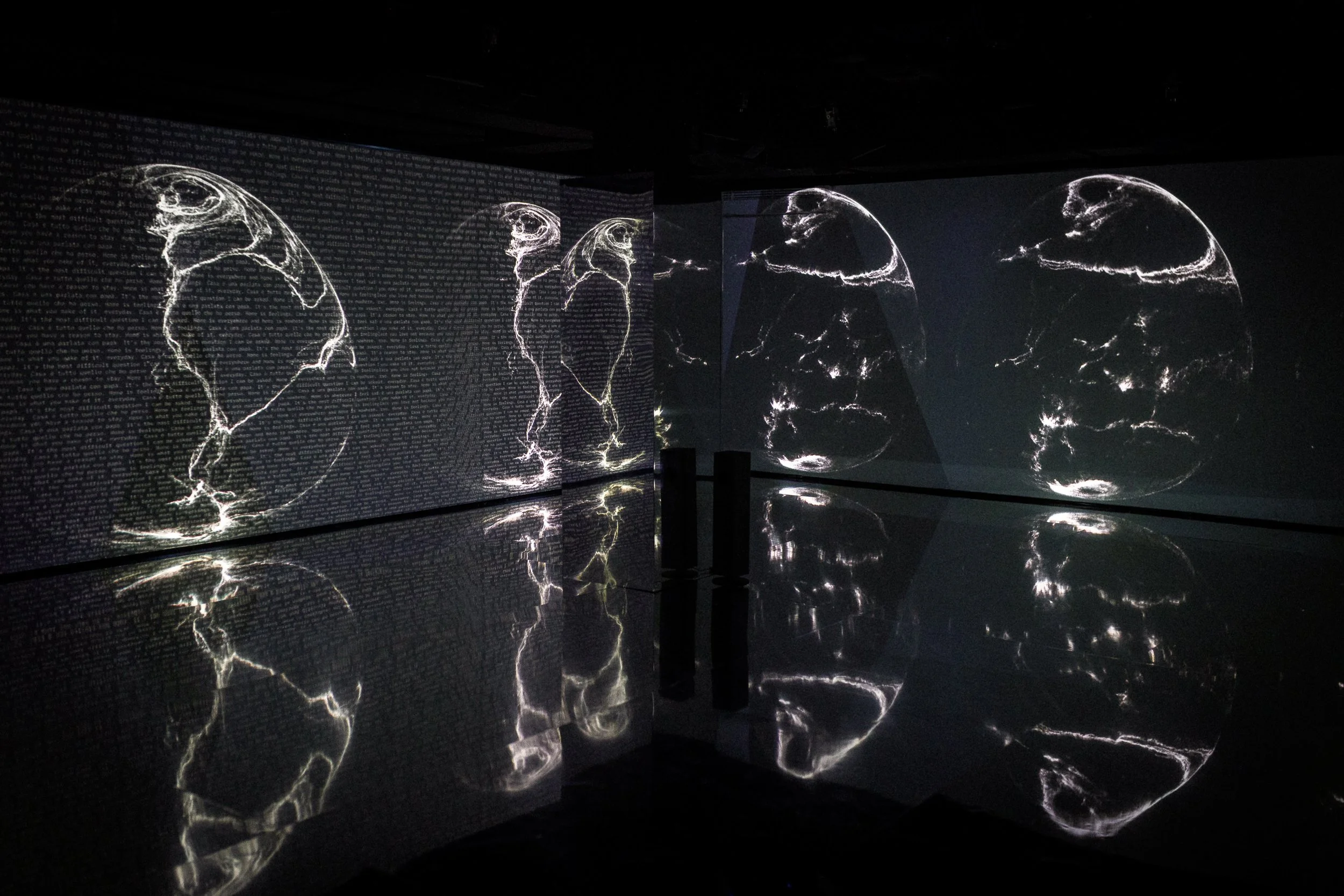 Dark room with illuminated line art of a face on multiple walls and reflections on the shiny floor, creating a mirrored effect.