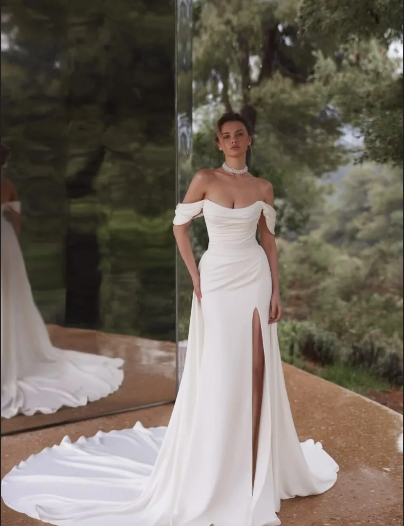 The Palace gown is a breathtaking mermaid-style masterpiece, expertly crafted from delicate satin. Its elegantly draped corset and off-the-shoulder sleeves evoke romance and sophistication. A high slit adds a hint of allure. With a flowing train that