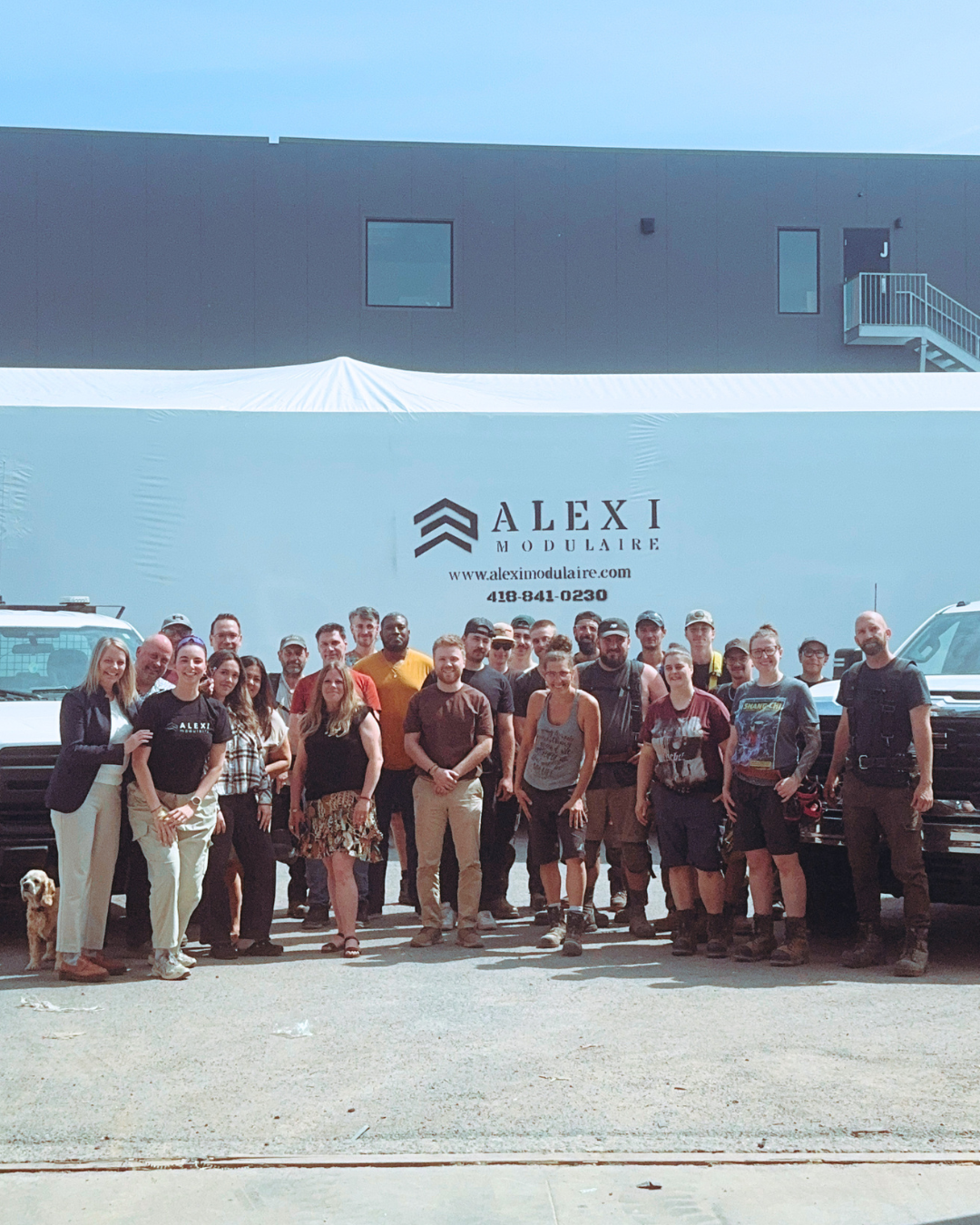 Équipe d’Alexi Modulaire posant devant un bâtiment modulaire, avec le logo et les coordonnées de l’entreprise visibles.