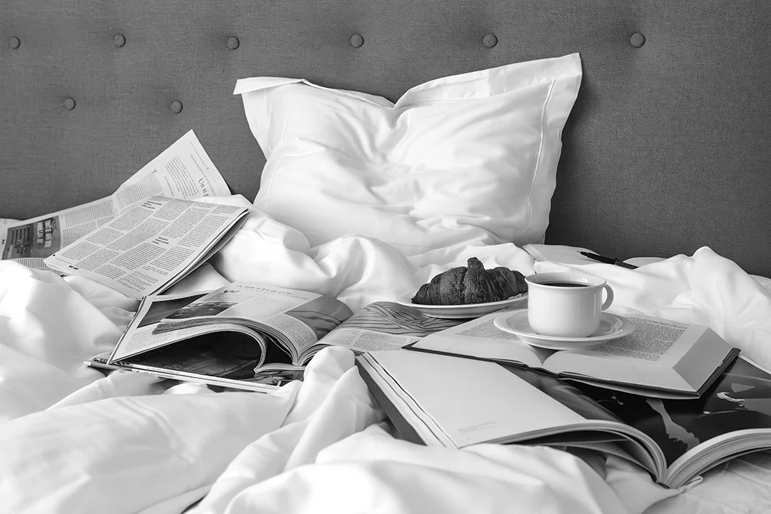 Stämningsfull svartvit fotokonst med frukost i sängen, böcker, kaffe och croissant. Ett elegant fotografi som förmedlar lugn, vardagslyx och modern fotokonst.