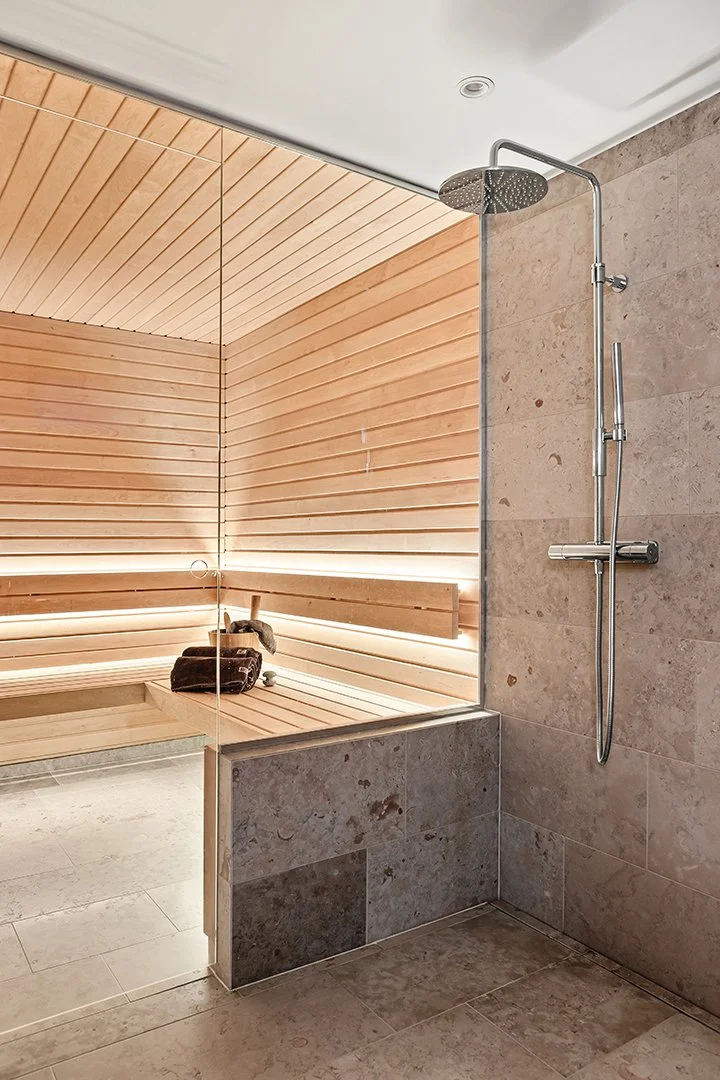 Interiörfoto av ett badrum i en vill på Lidingö. Kalksten på väggar och golv samt en bastu med glasfront.