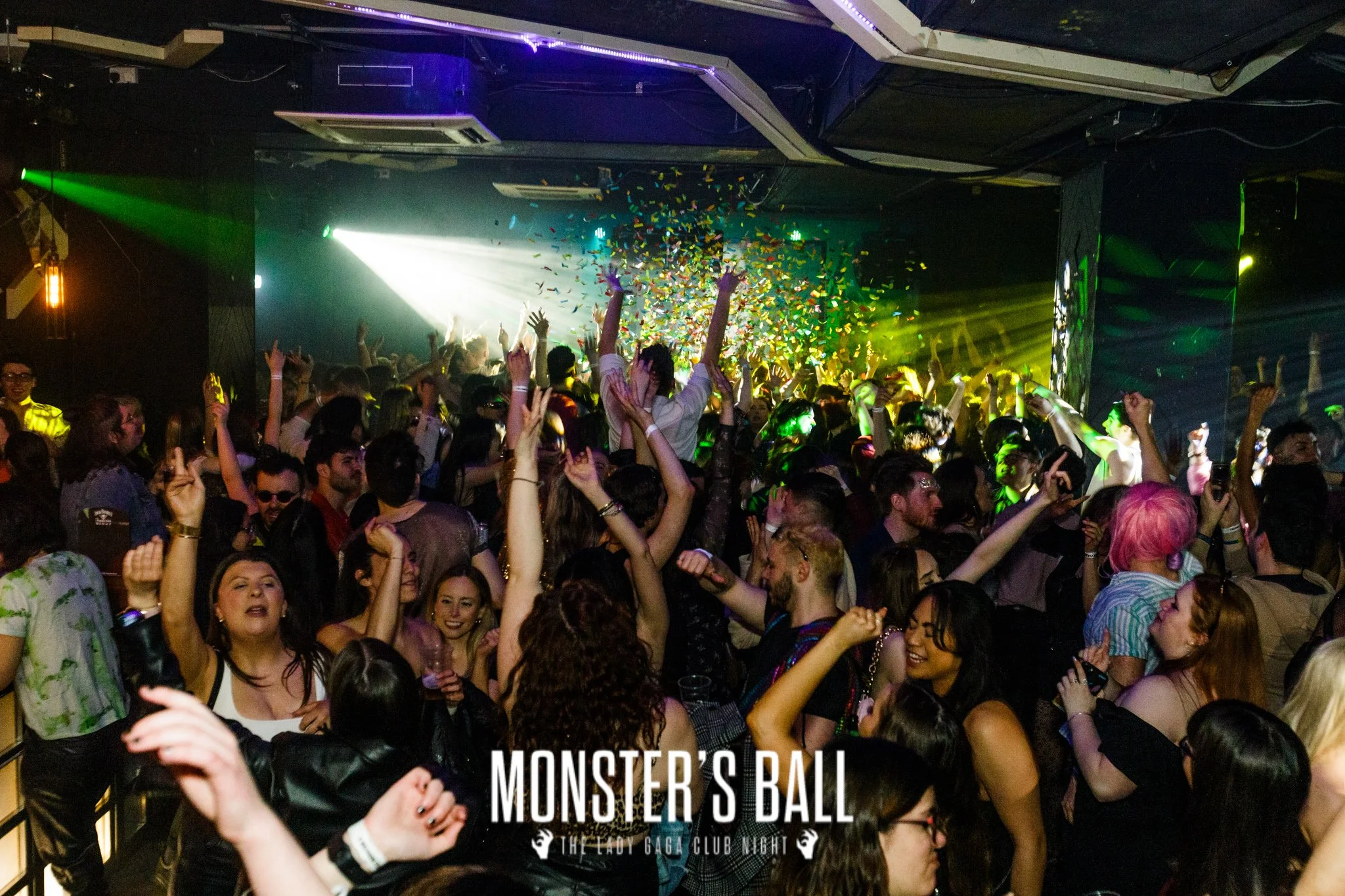 Crowd dancing and celebrating at a nightclub event with confetti and colorful lights, labeled "MONSTER'S BALL" at the bottom.