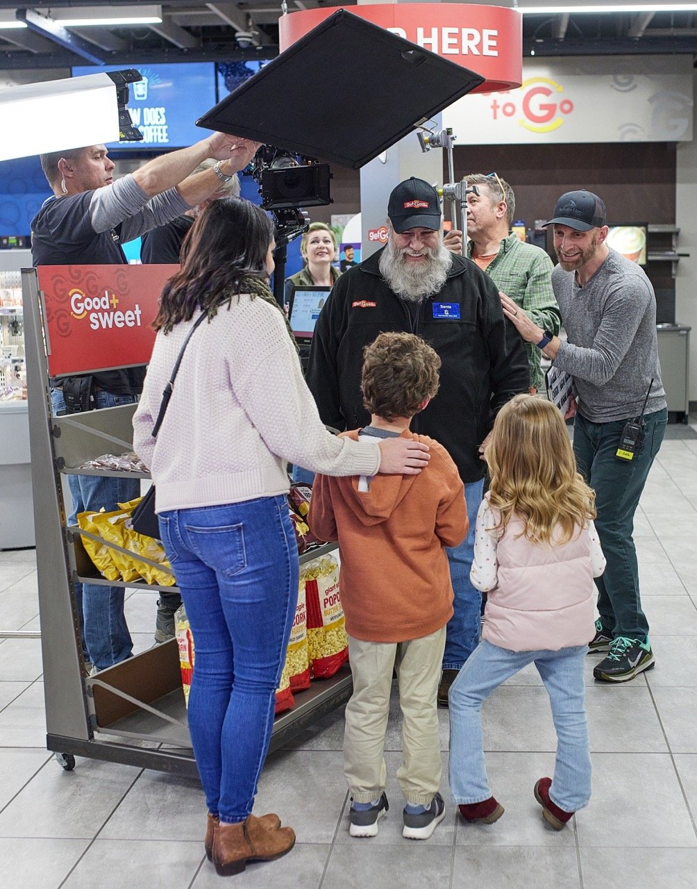 A behind-the-scenes photo of a commercial film set in a store, with a crew setting up lights and cameras.