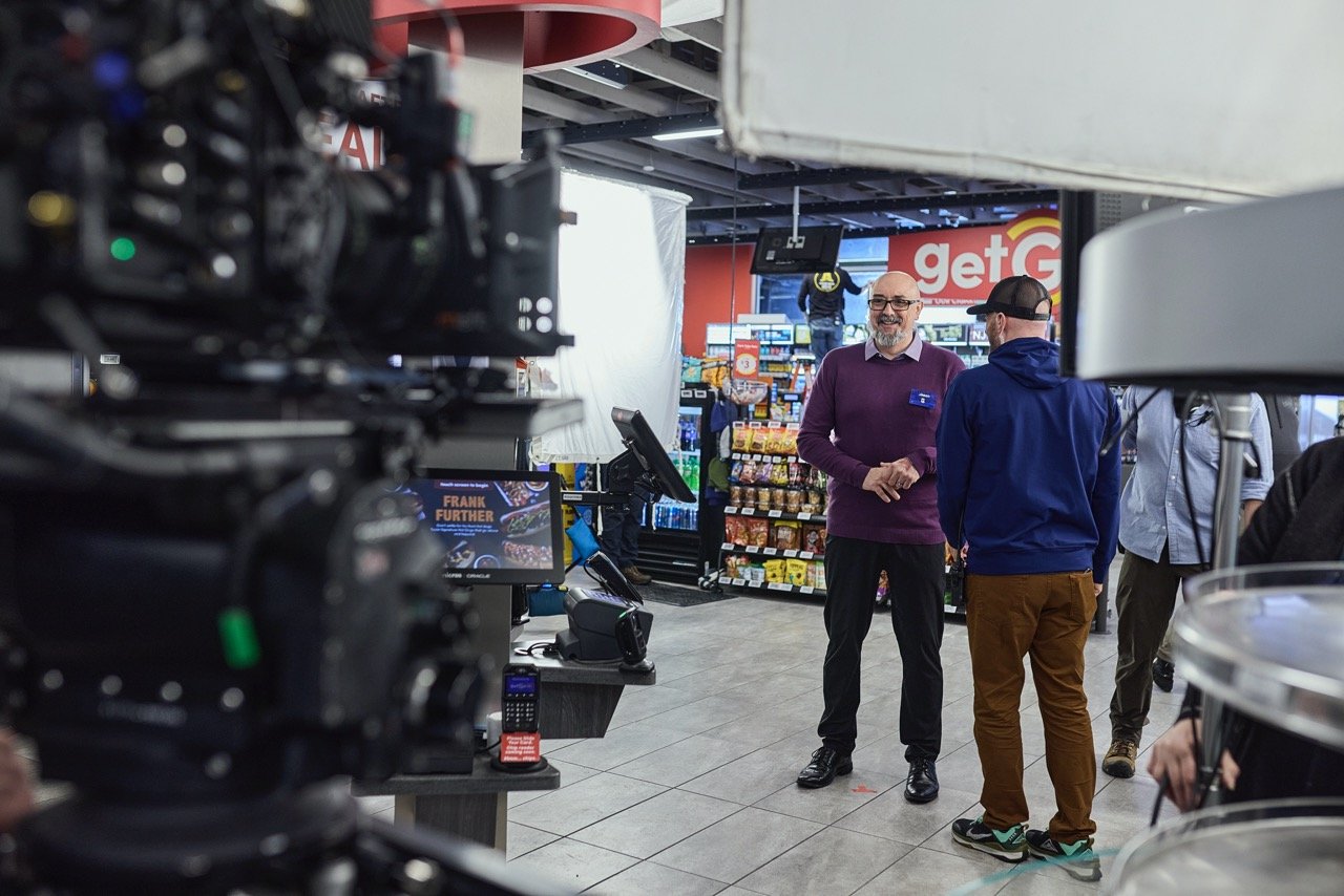A commercial film crew recording a scene inside a convenience store.