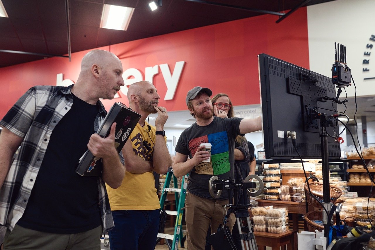 Director, assistant director, and director of photography reviewing footage on a monitor in a bakery setting.