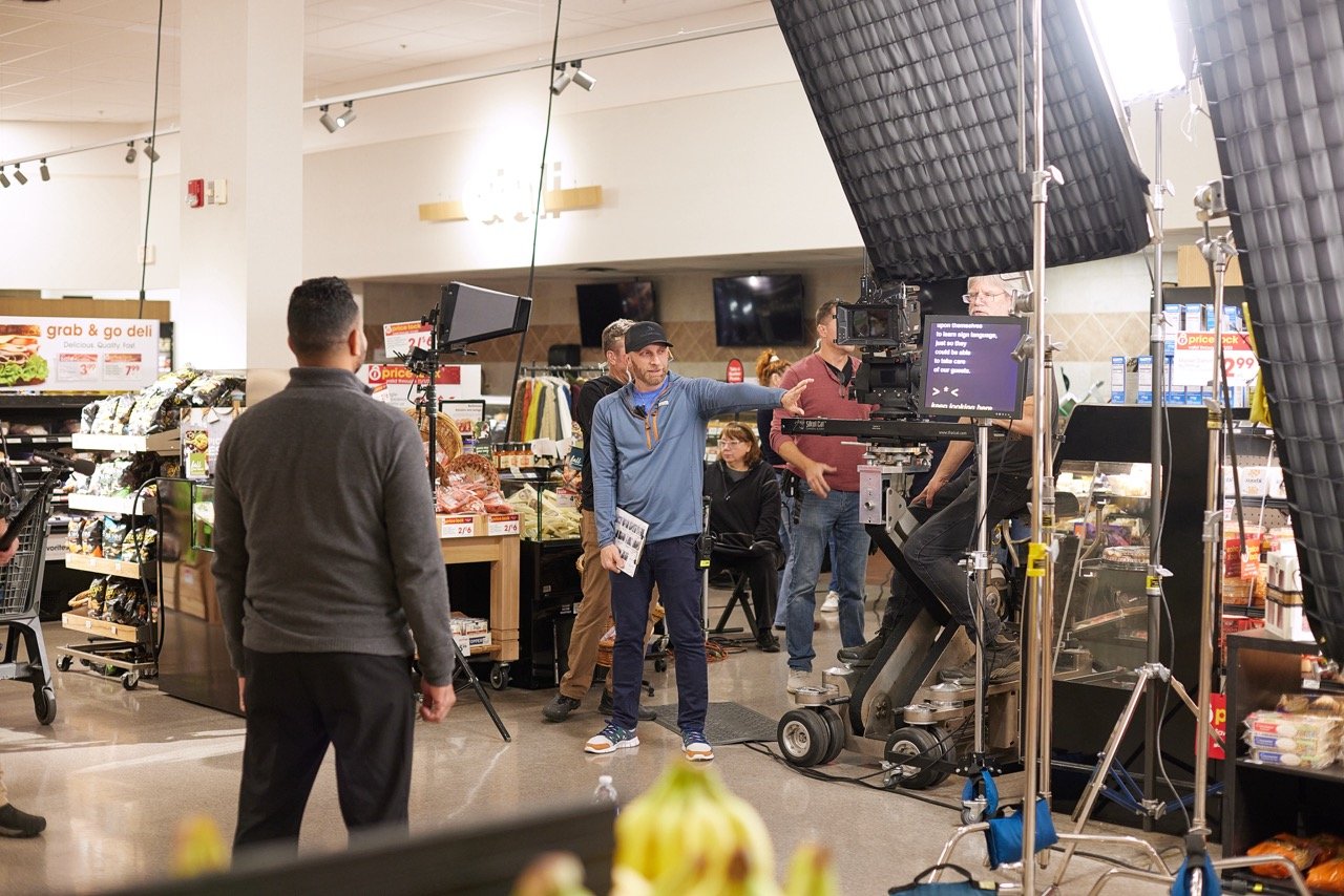 Commercial film crew setting up a scene in a grocery store with lighting and camera equipment.