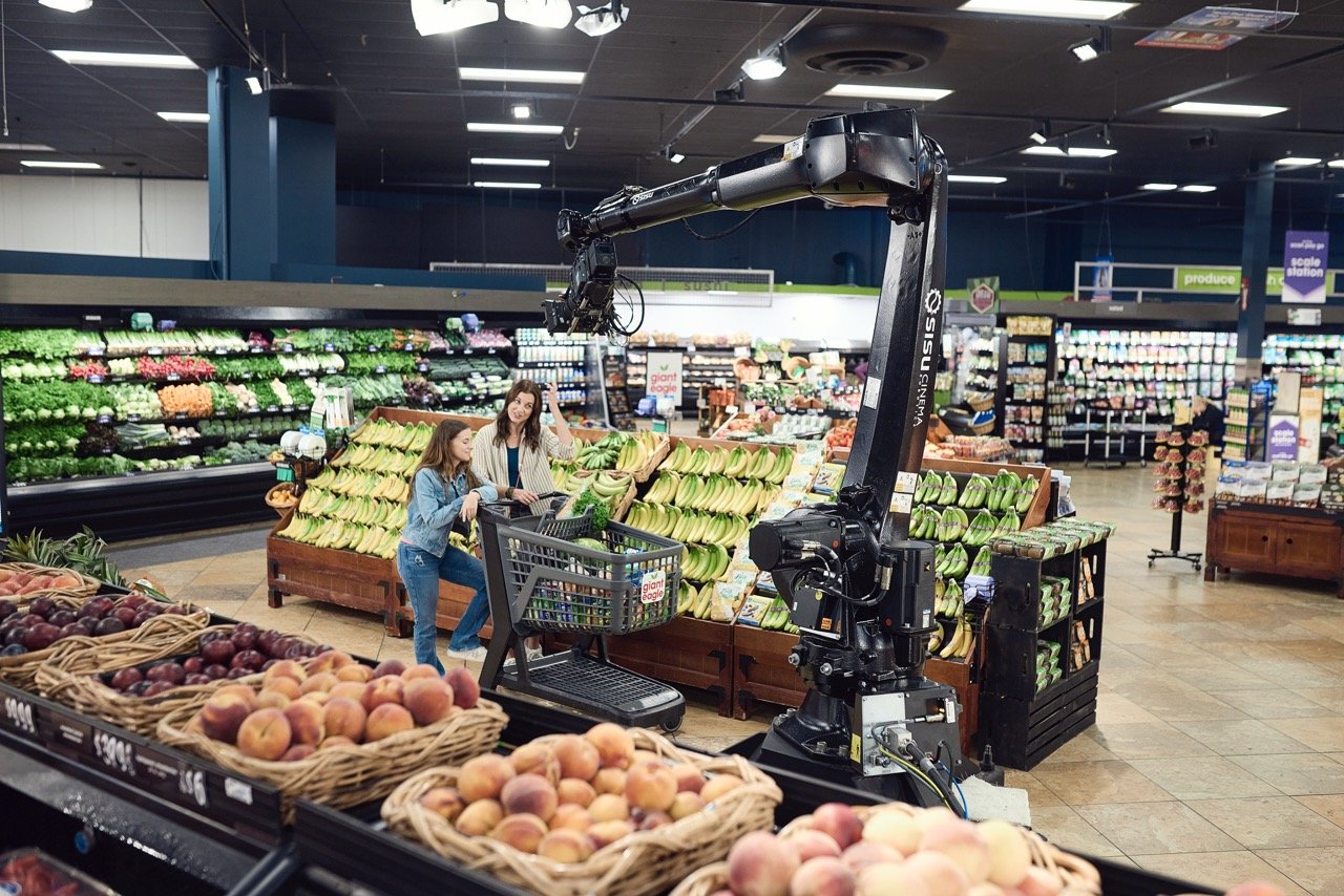 Talent in a supermarket produce section, with a robotic camera crane filming them near shelves of fruits and vegetables.