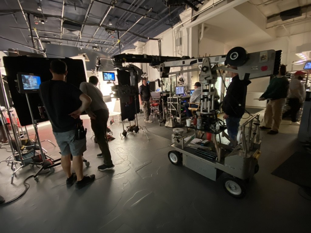 Commercial film crew working in studio with equipment, cameras, and monitors on a tabletop commercial set.