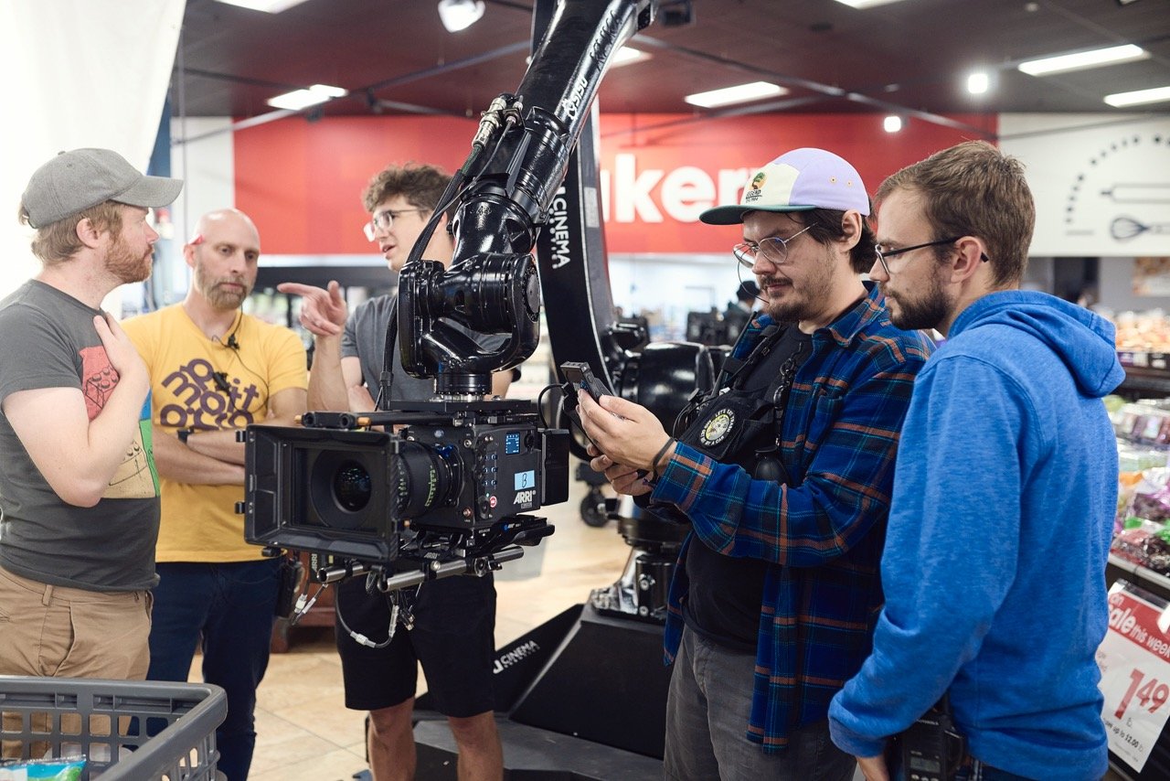 Group of people around a professional movie camera on a set in a supermarket.