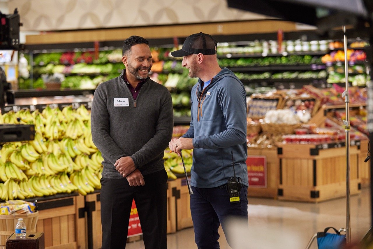 Director and talent talking in a grocery store produce section during TV commercial production.