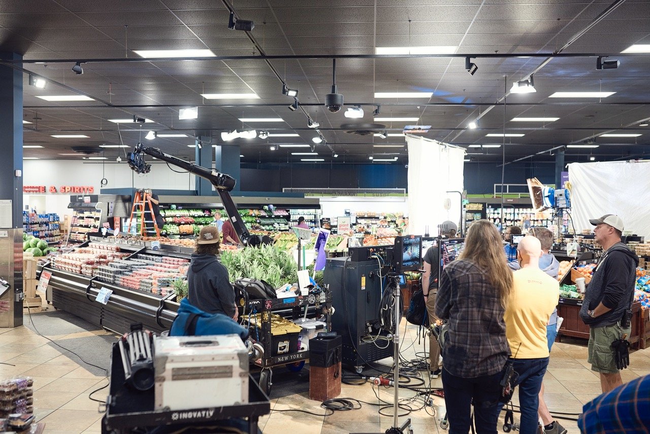 Film crew setting up equipment in a grocery store's produce section.