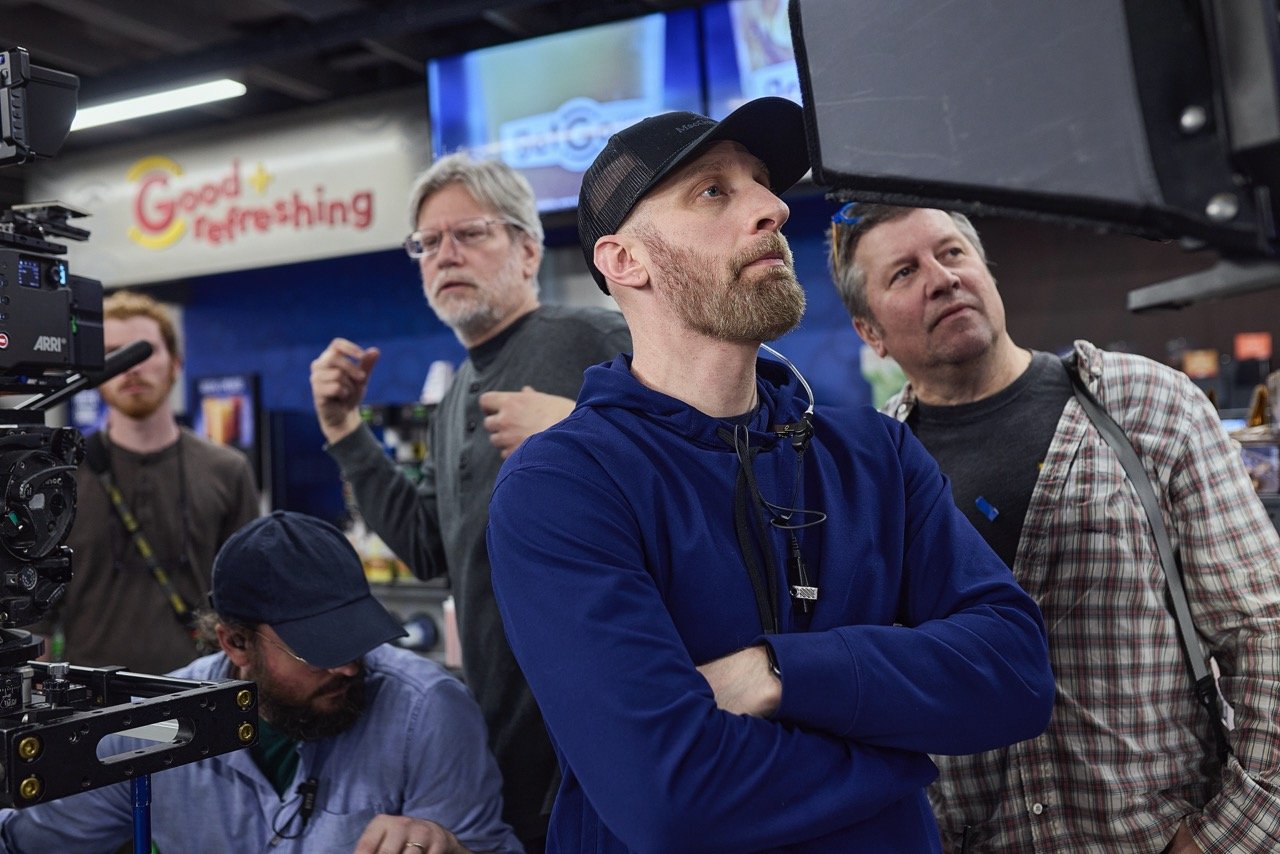Director & gaffer on a commercial film set observing a camera monitor, inside a convenience store setting.