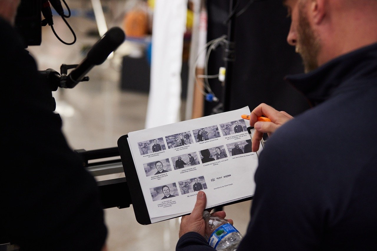 Director holding a storyboard on a clipboard, with a pen and water bottle, near camera equipment.