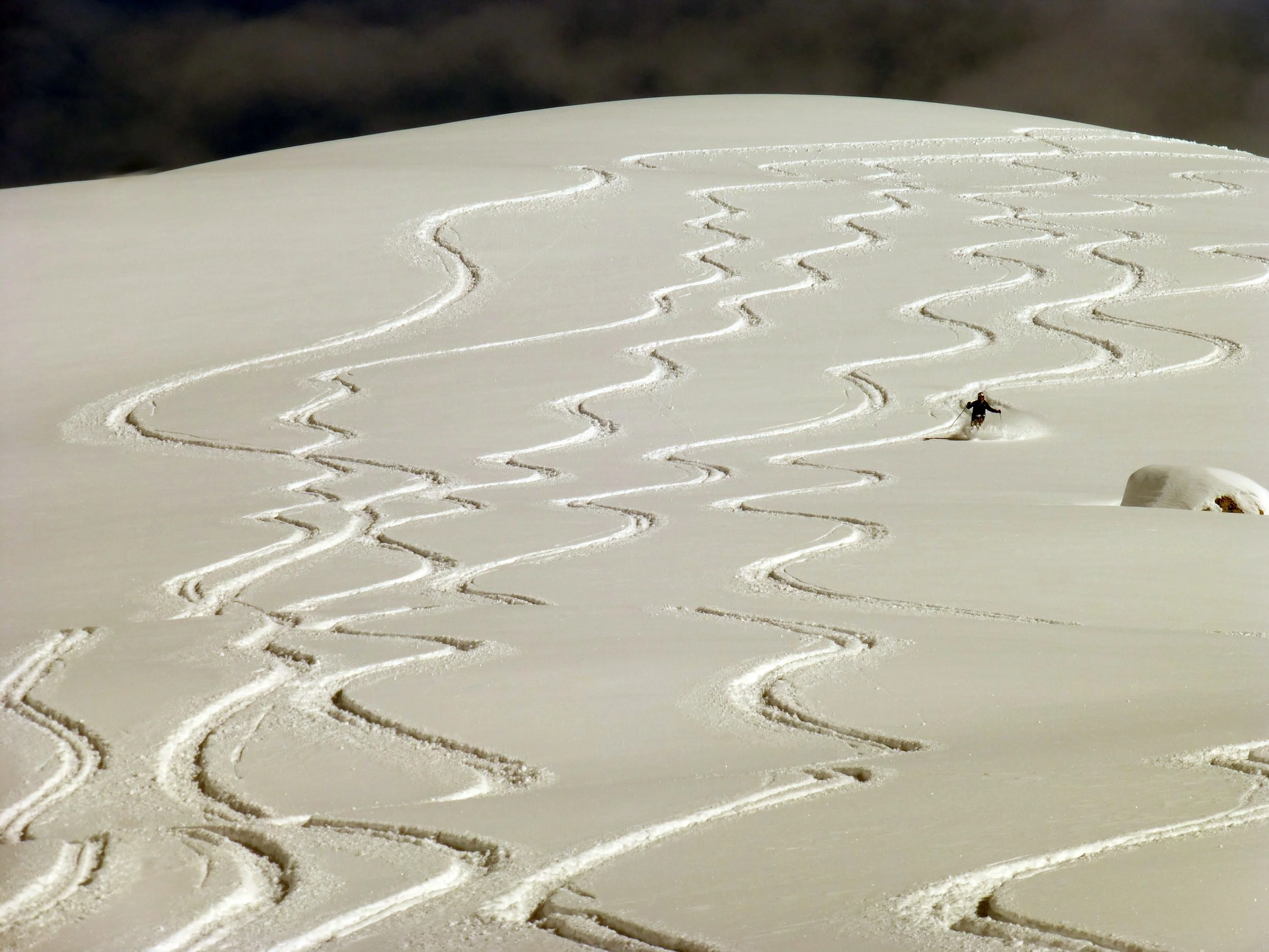 Ski tracks in the snow on a mountain slope with a skier in the distance.