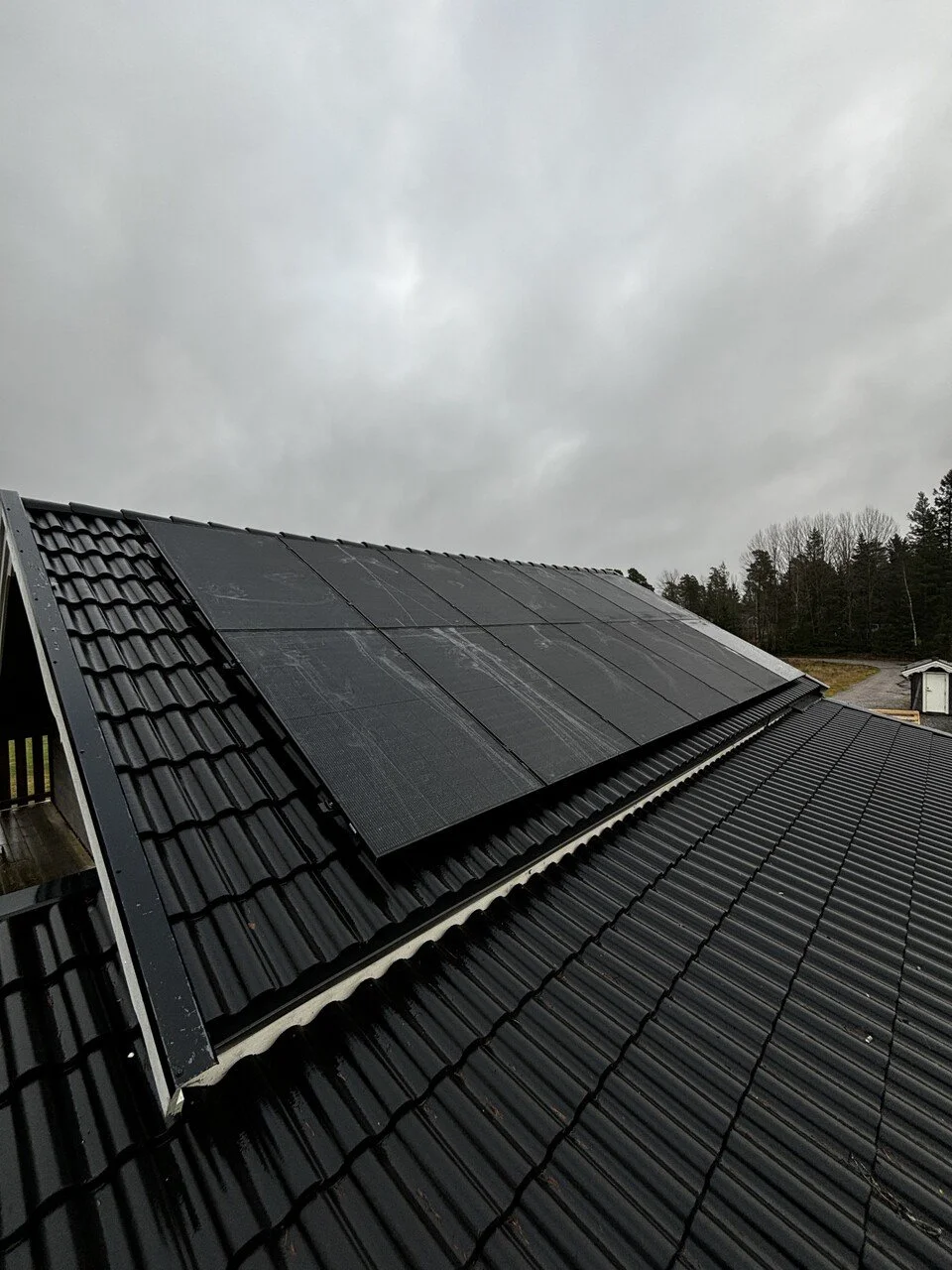 Tak med solpaneler på en villa i dimmigt landskap med träd och andra hus i bakgrunden.