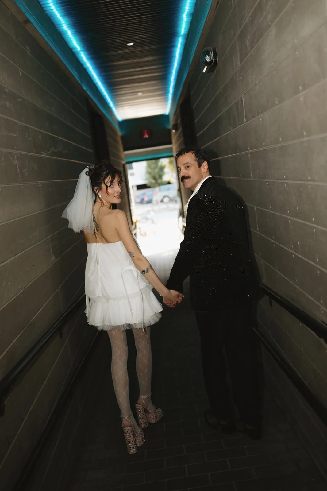  Newlyweds holding hands and looking back over their shoulders as they walk through a tunnel 