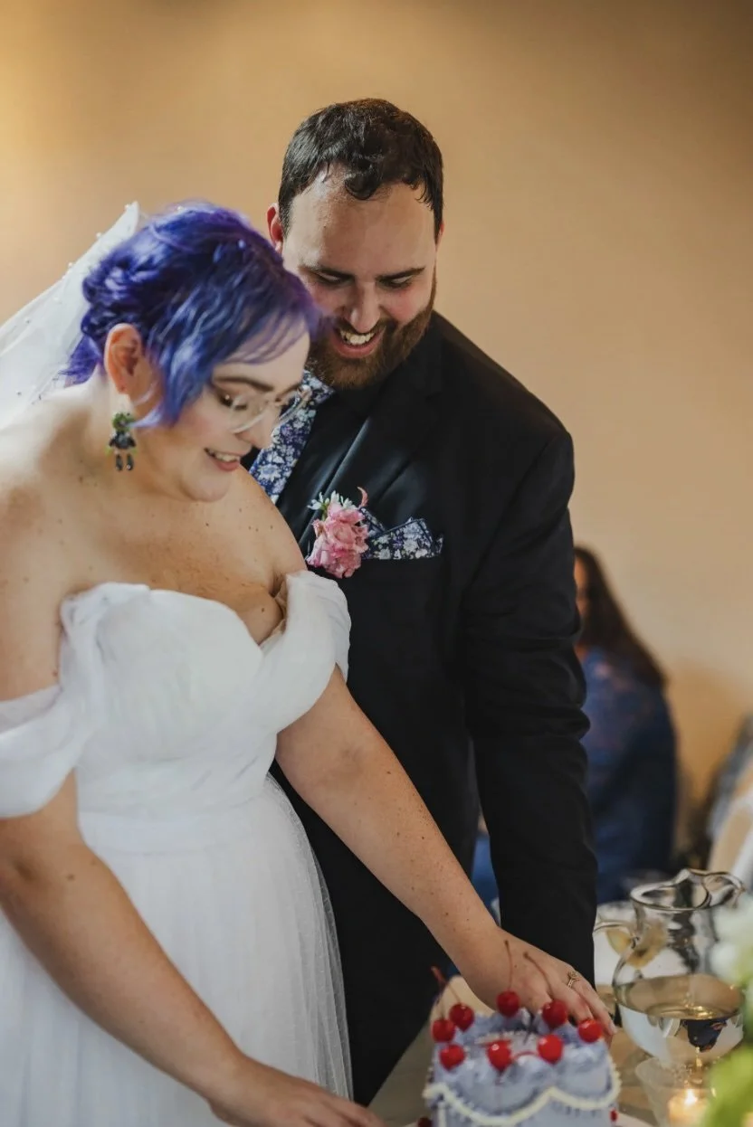 A newlywed couple reaching in to cut their wedding cake