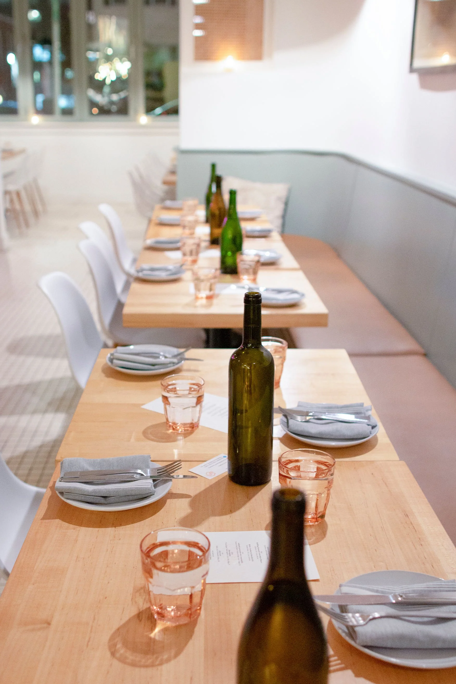 Bottles and flatware set up on small tables at a restaurant 