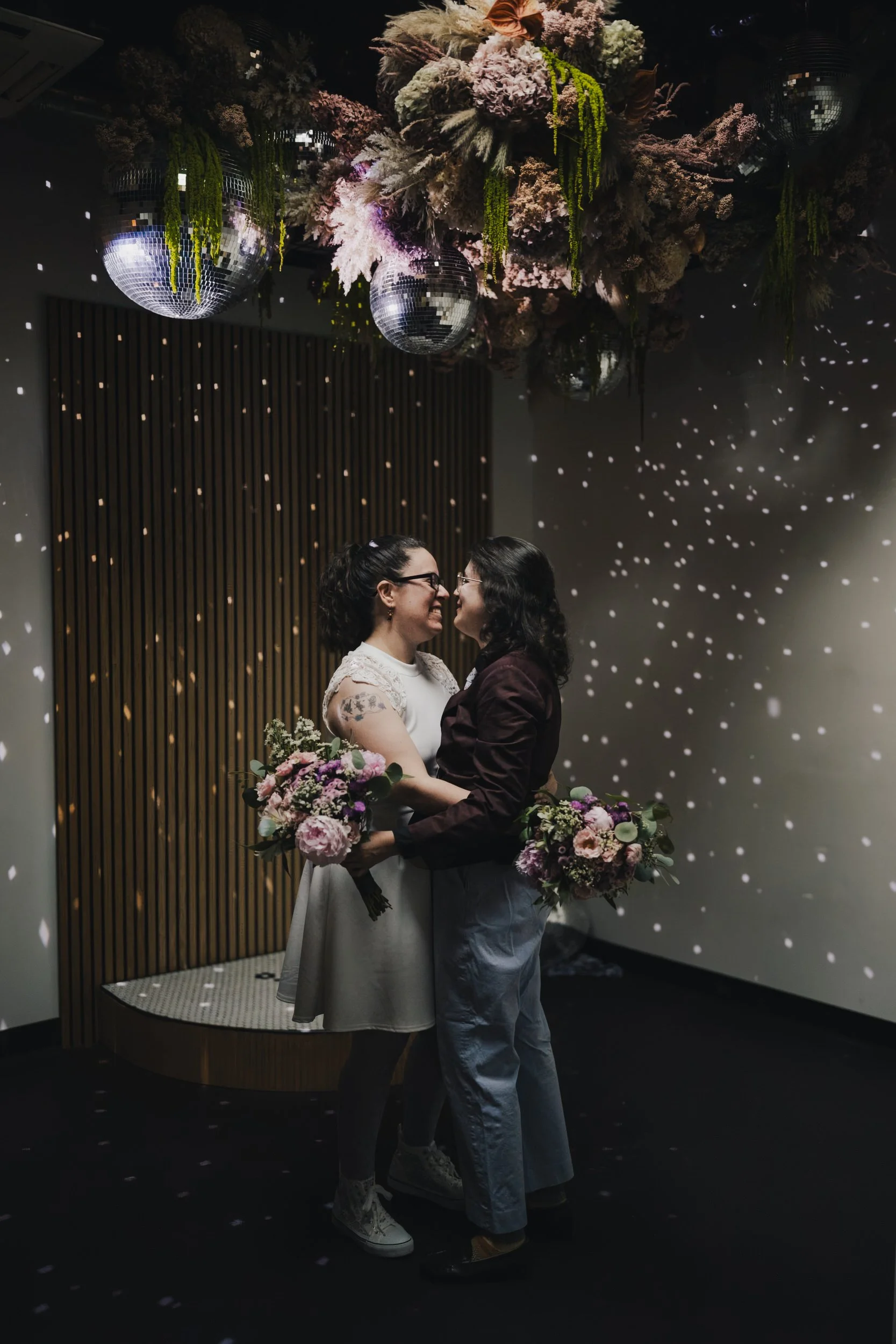  Newlyweds with their arms around each other’s waists standing under disco lights 
