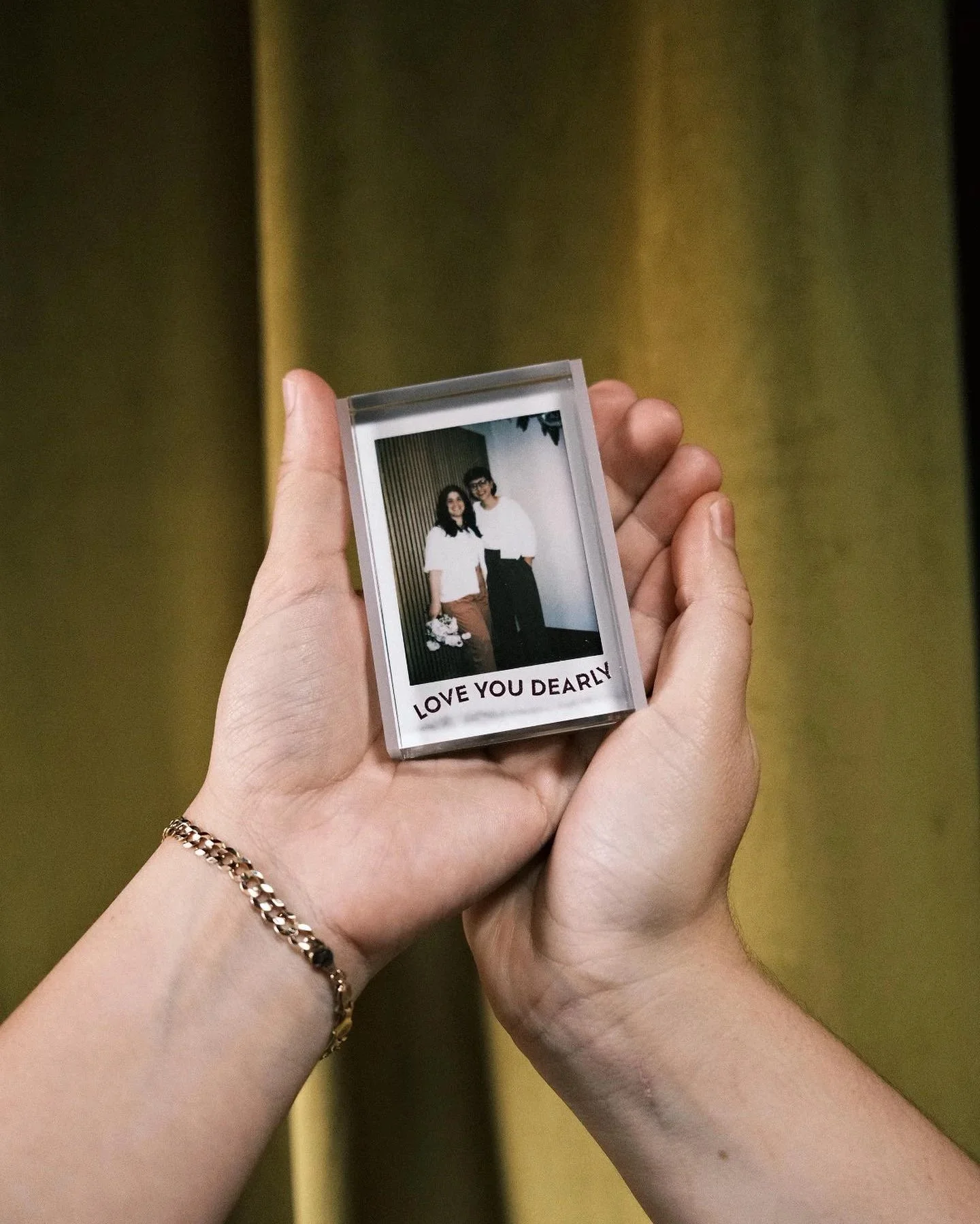 A person holding a small transparent photo frame with a picture of a couple and the words 'LOVE YOU DEARLY' at the bottom.