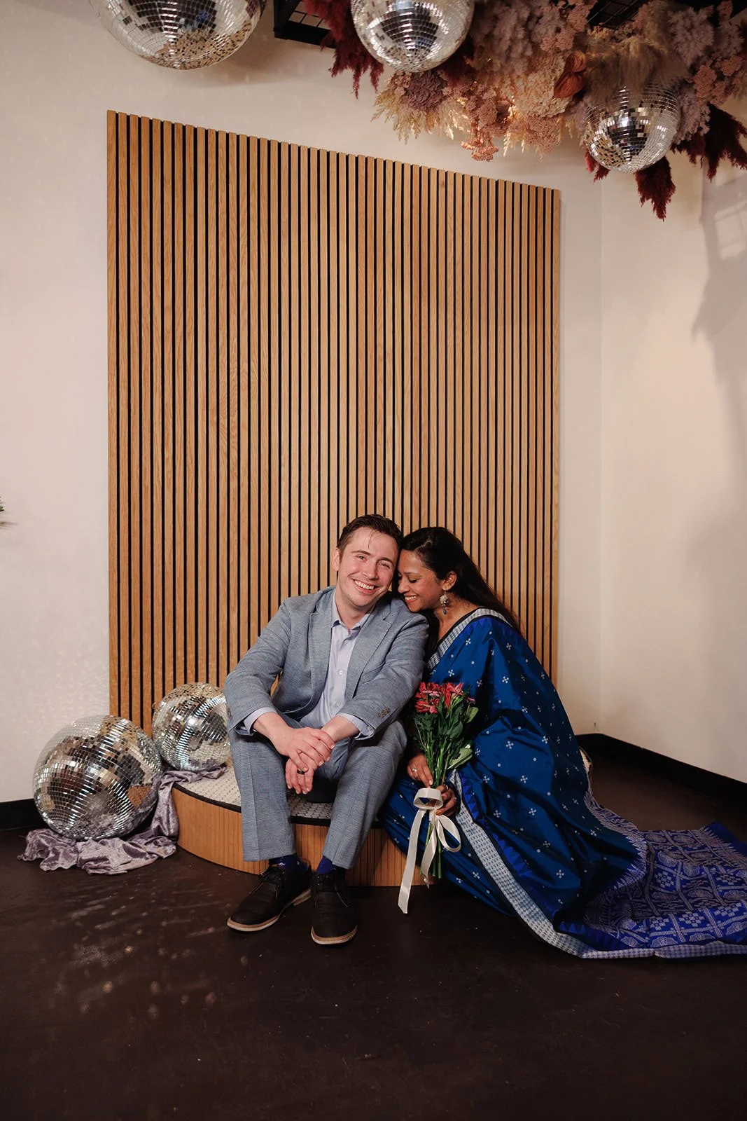  Newlyweds sitting on a small wedding ceremony platform as they lean into each other and smile  