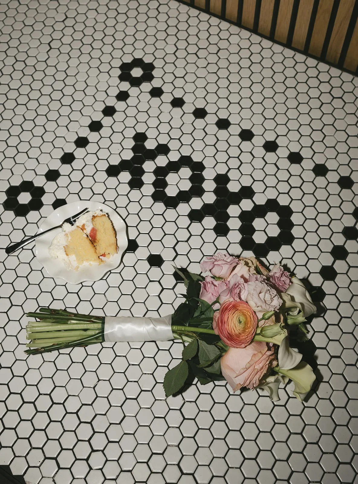  A bouquet and a piece of cake laid on a tile floor with a design in it that reads “xoxo” 