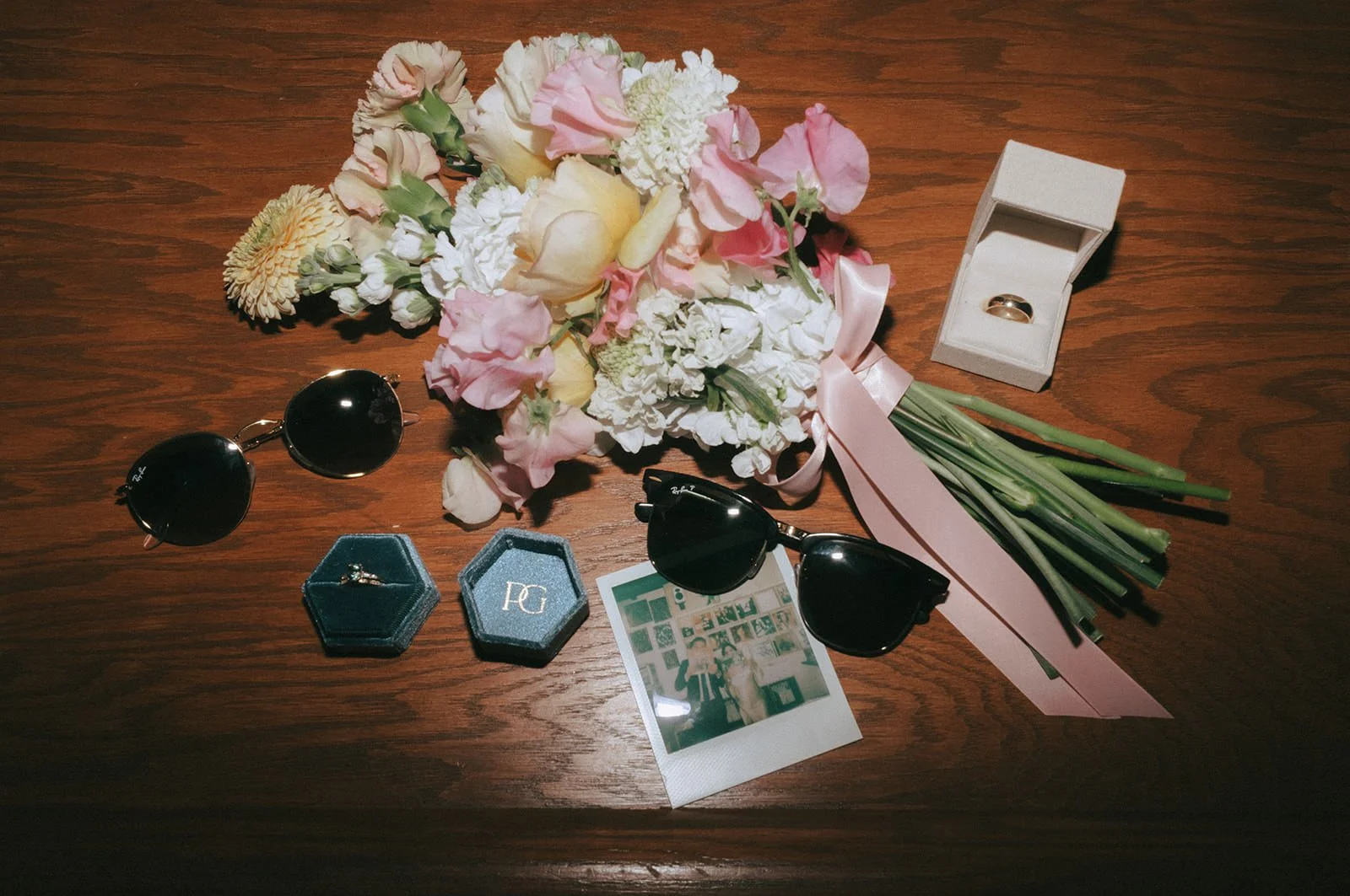  A flat lay photo with sunglasses, polaroids, wedding rings, and a bouquet of flowers 