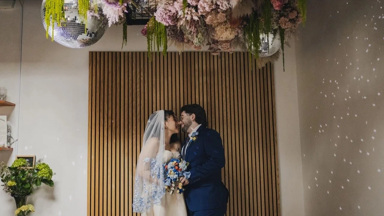  Two people face each other and smile, about to kiss. It appears to be their wedding day. 