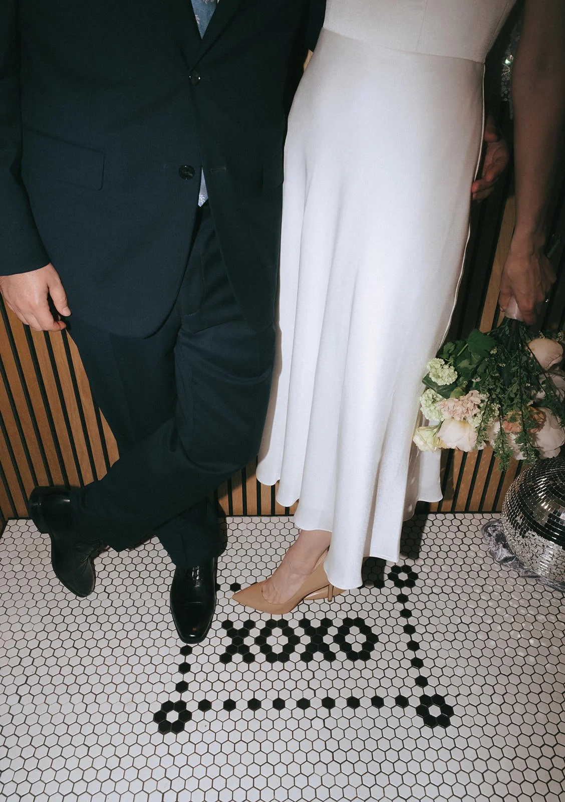 A newlywed couple standing on a tile floor with "xoxo" under their feet.