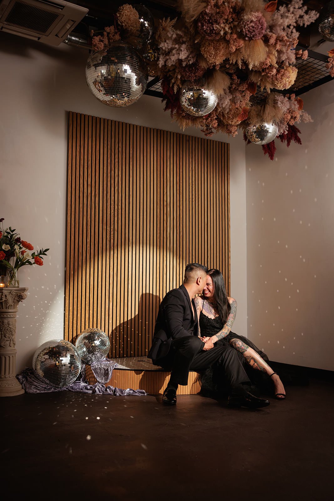 Newlyweds sitting on a platform under a spotlight as they kiss
