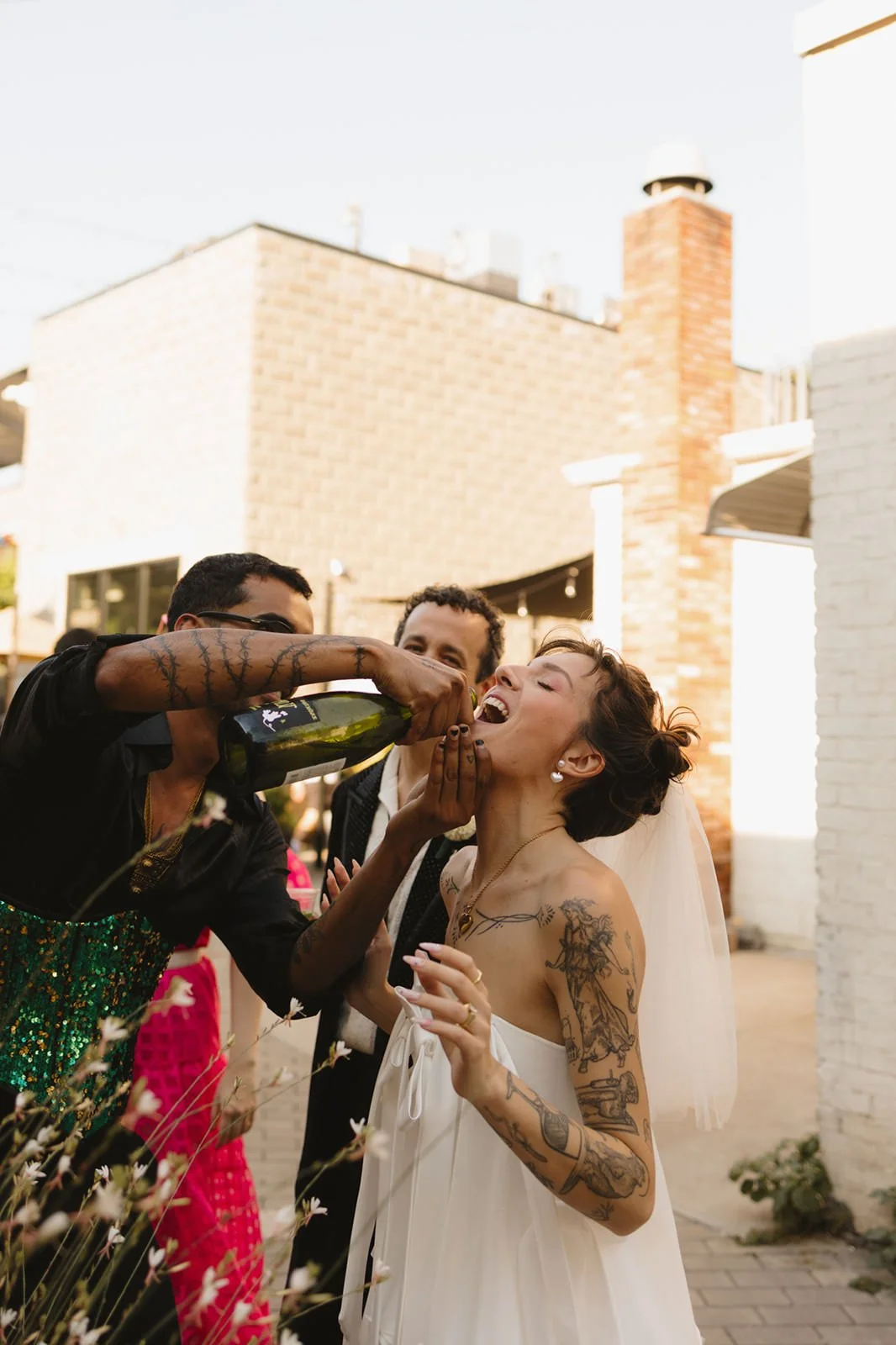 A person pouring champagne directly into a newlywed's mouth from a bottle