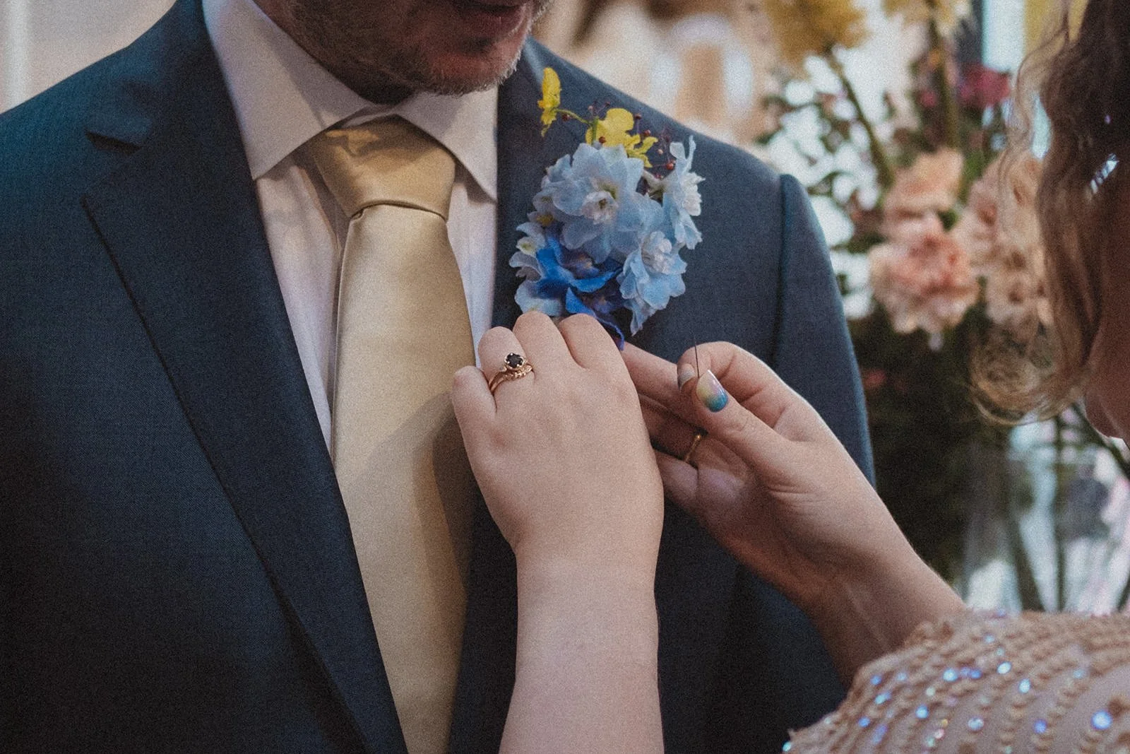 A person helping to pin a boutonniere on their partner's suit jacket