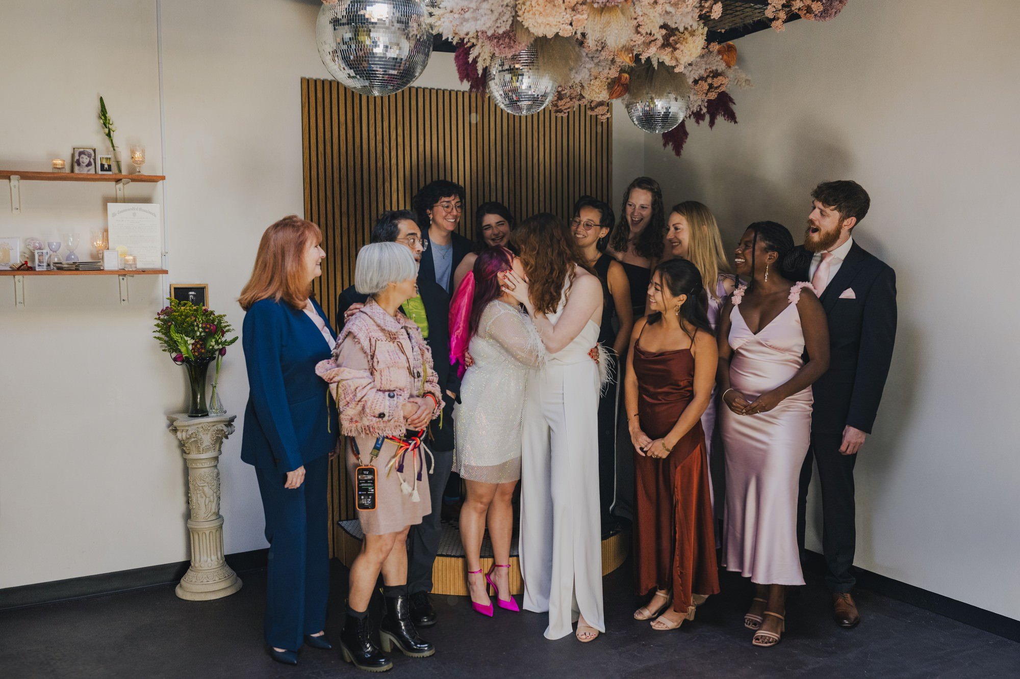 Newlyweds kissing as their family stand around them smiling