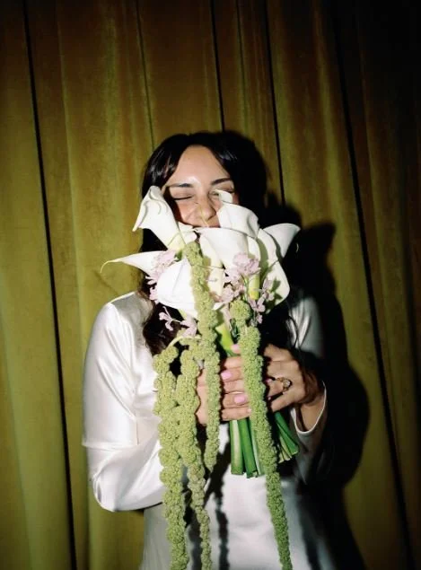 A newlywed smiling as they hold flowers up in front of their face
