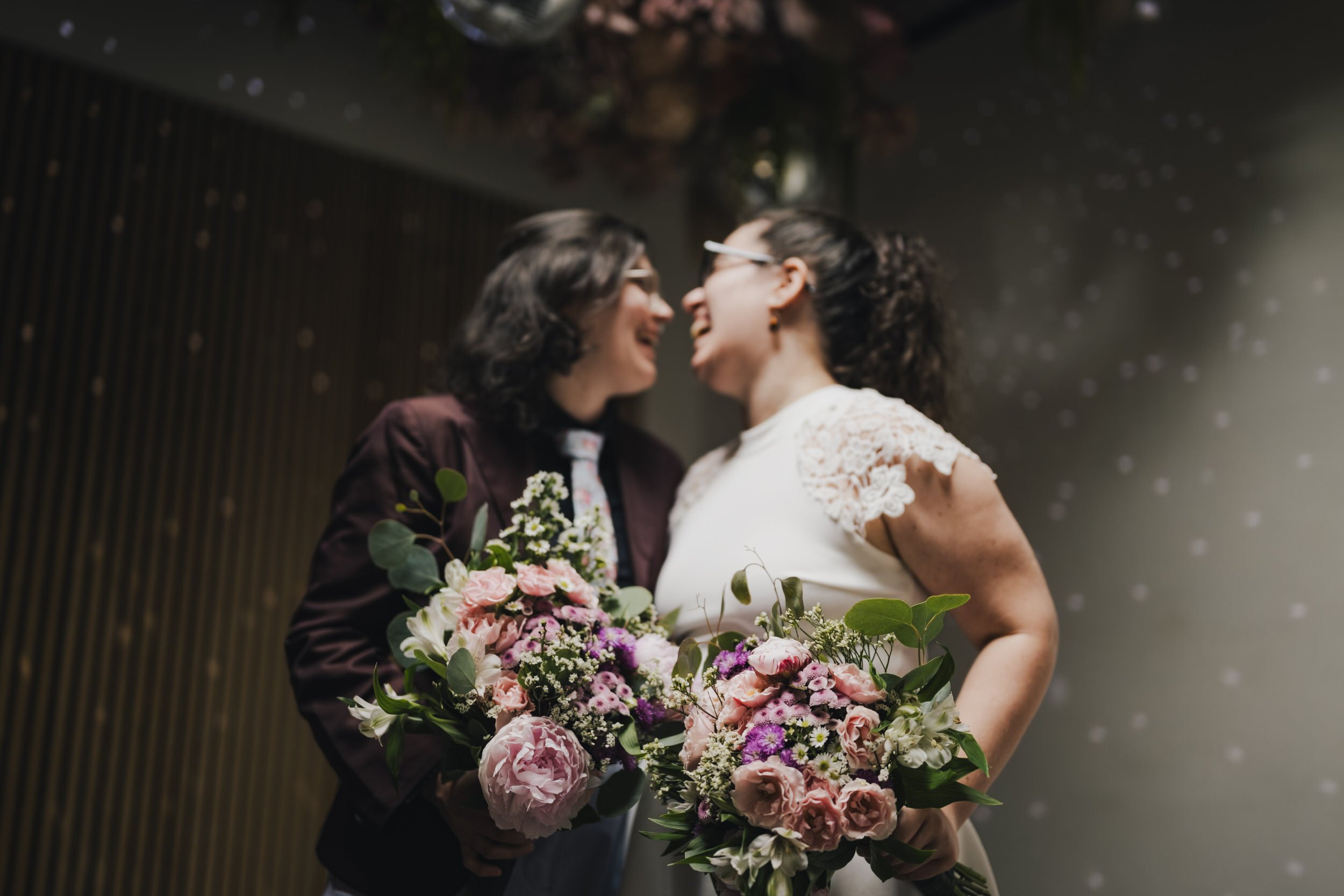  Newlyweds smiling as they lean in to kiss while they both hold bouquets of flowers 