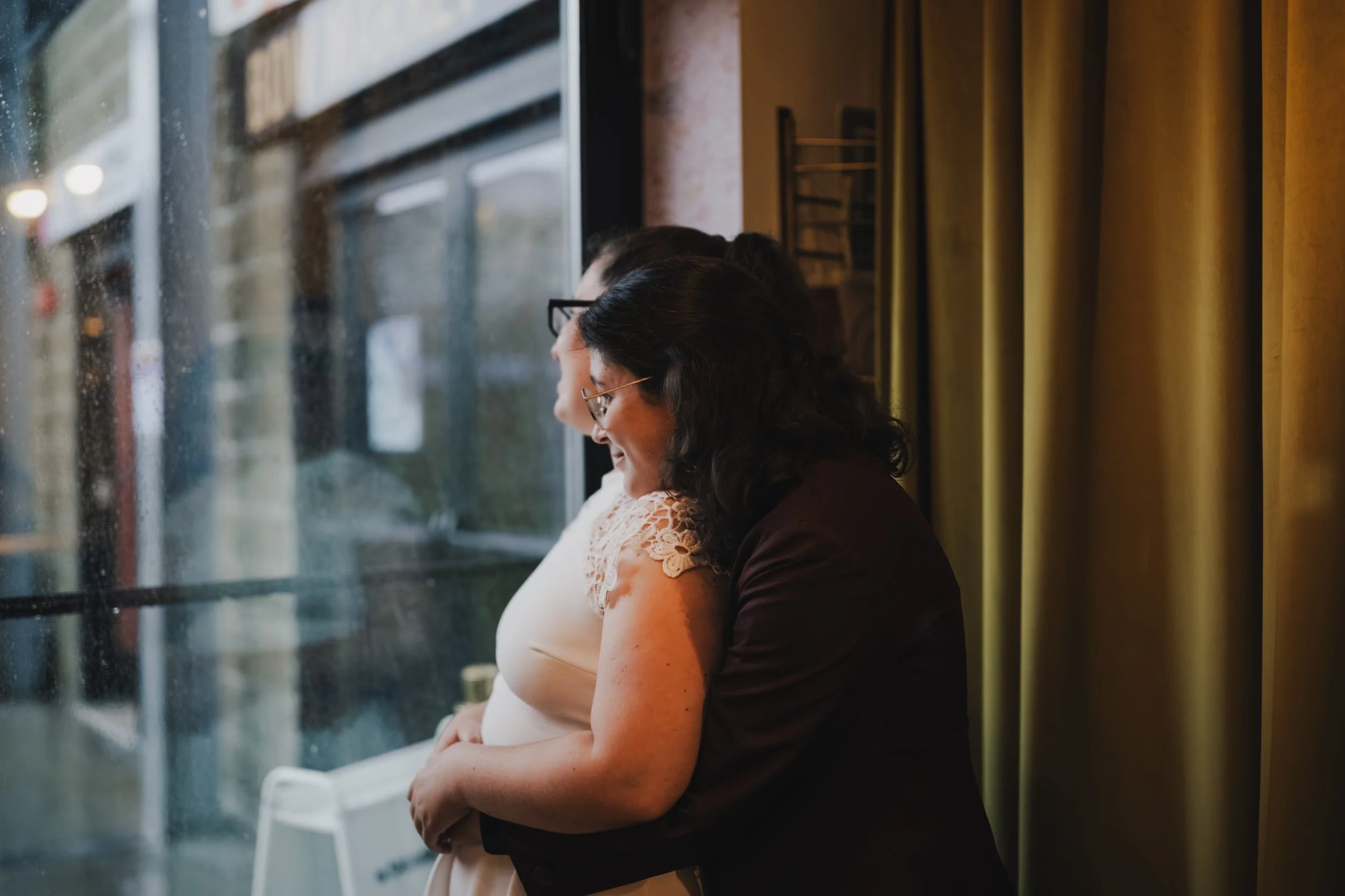 A newlywed hugging their partner from behind as they look out a window