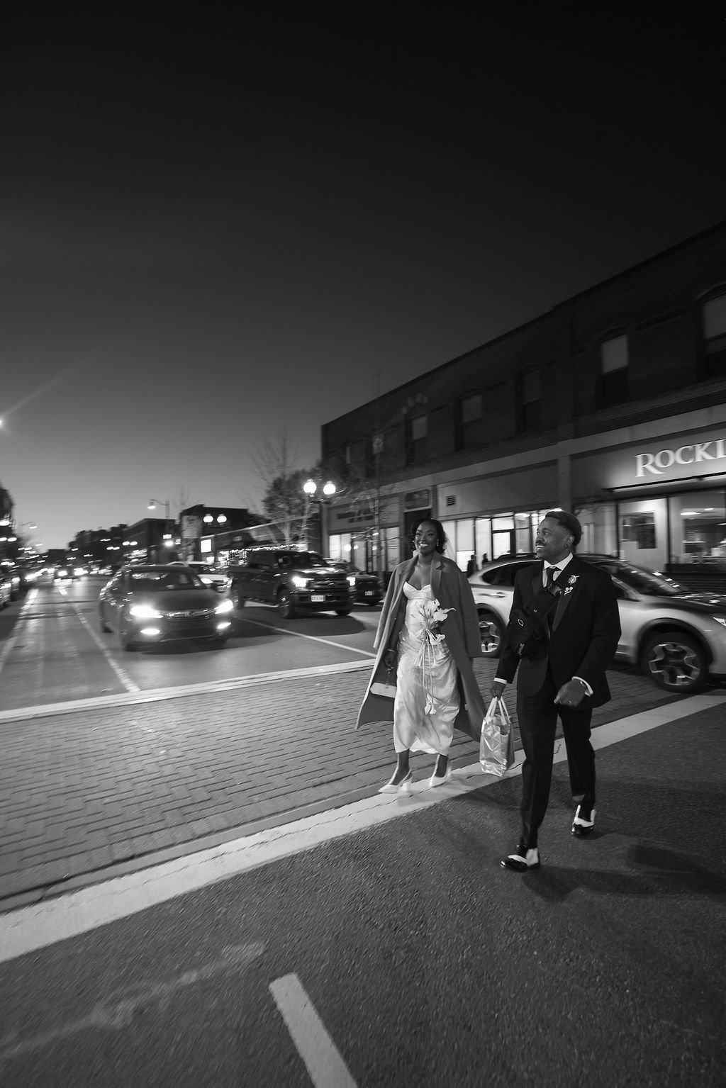 Newlyweds walking across a city street at night