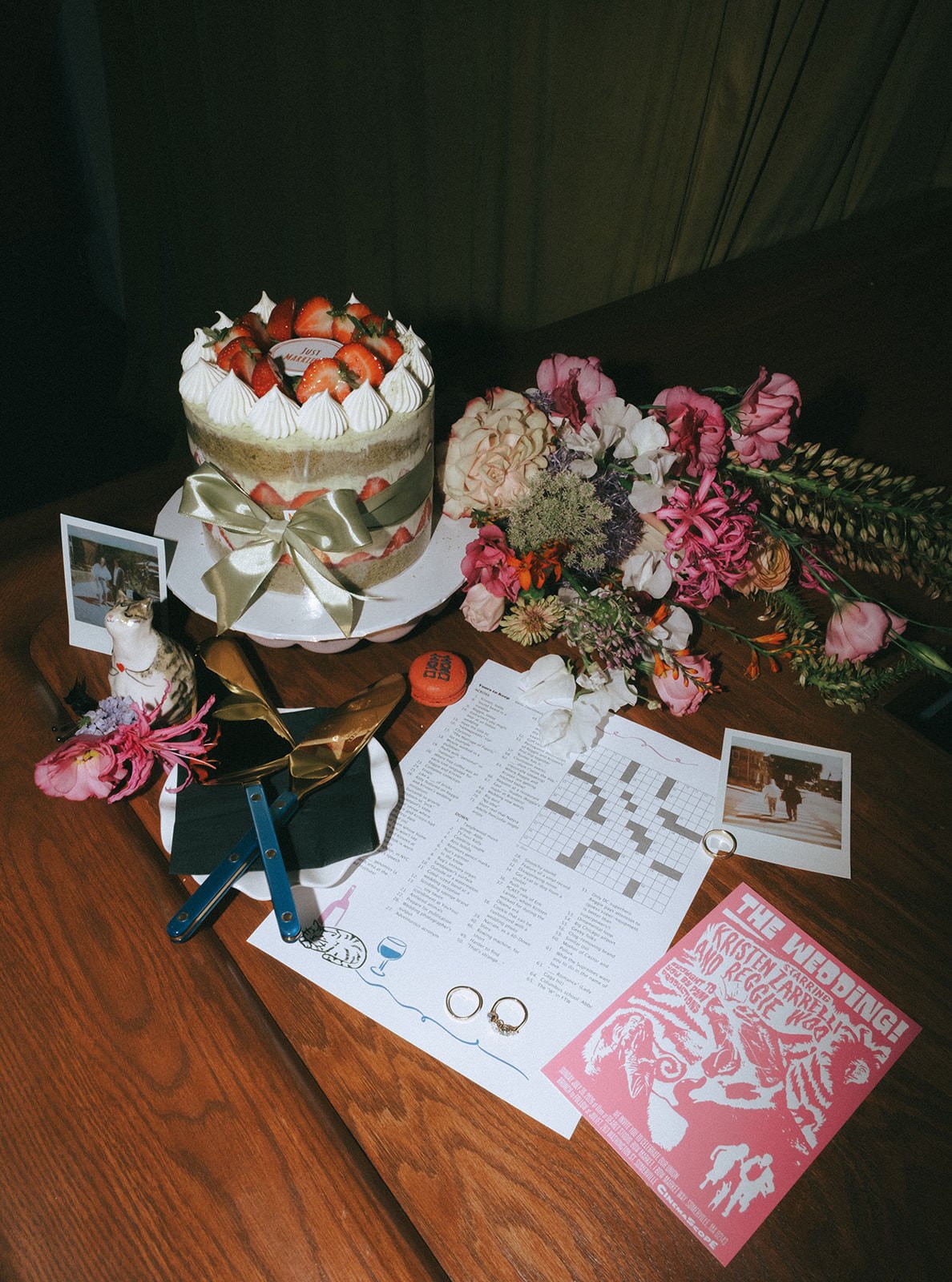 A wedding cake sitting next to a bouquet of flowers, jewelry, rings, polaroids, and other wedding favors