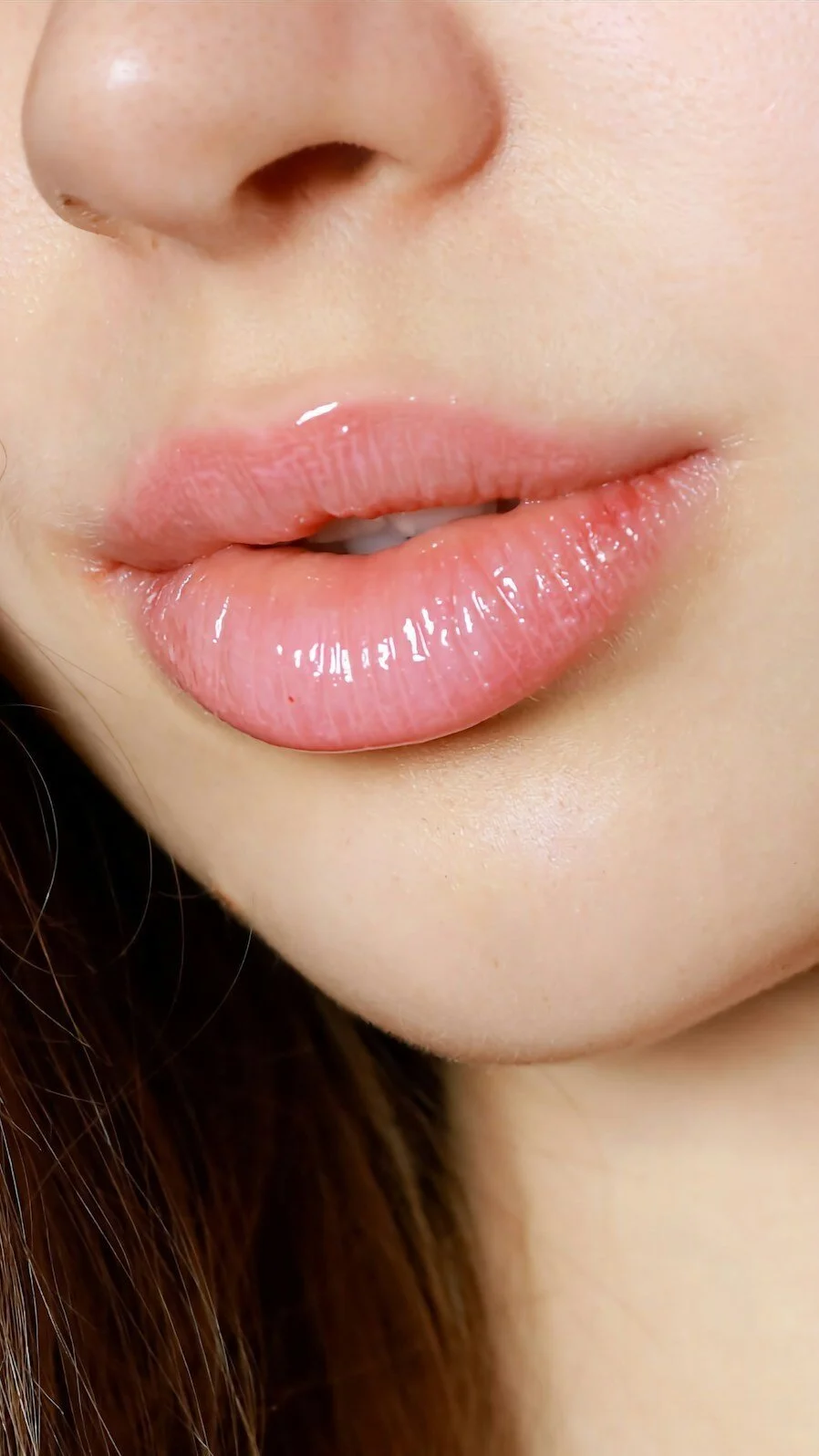 Close-up of a person's lips with glossy pink lipstick, partially open, and a small nose.