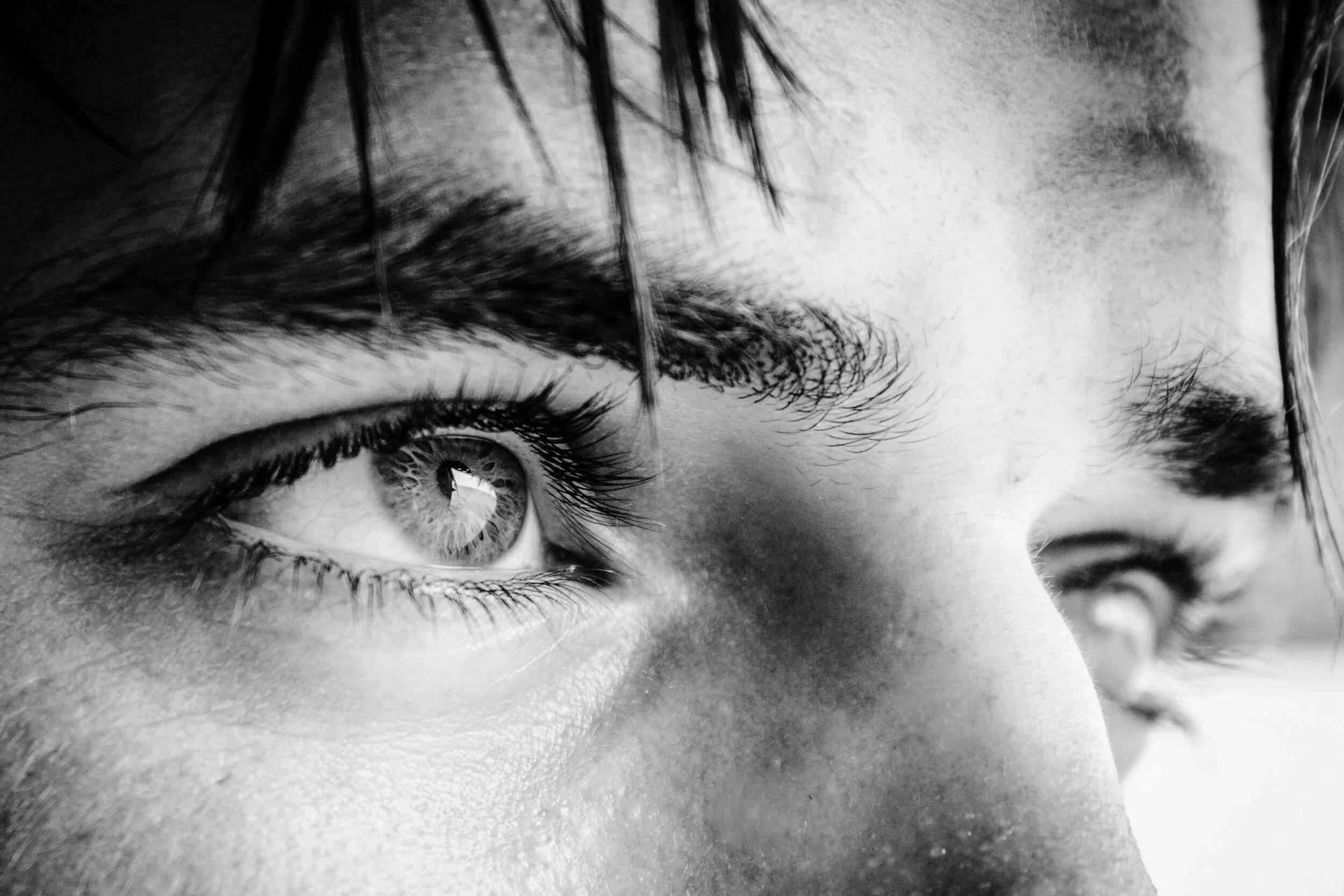 Close-up black and white photo of a person's eyes and part of their face, focusing on detailed eye and skin texture.