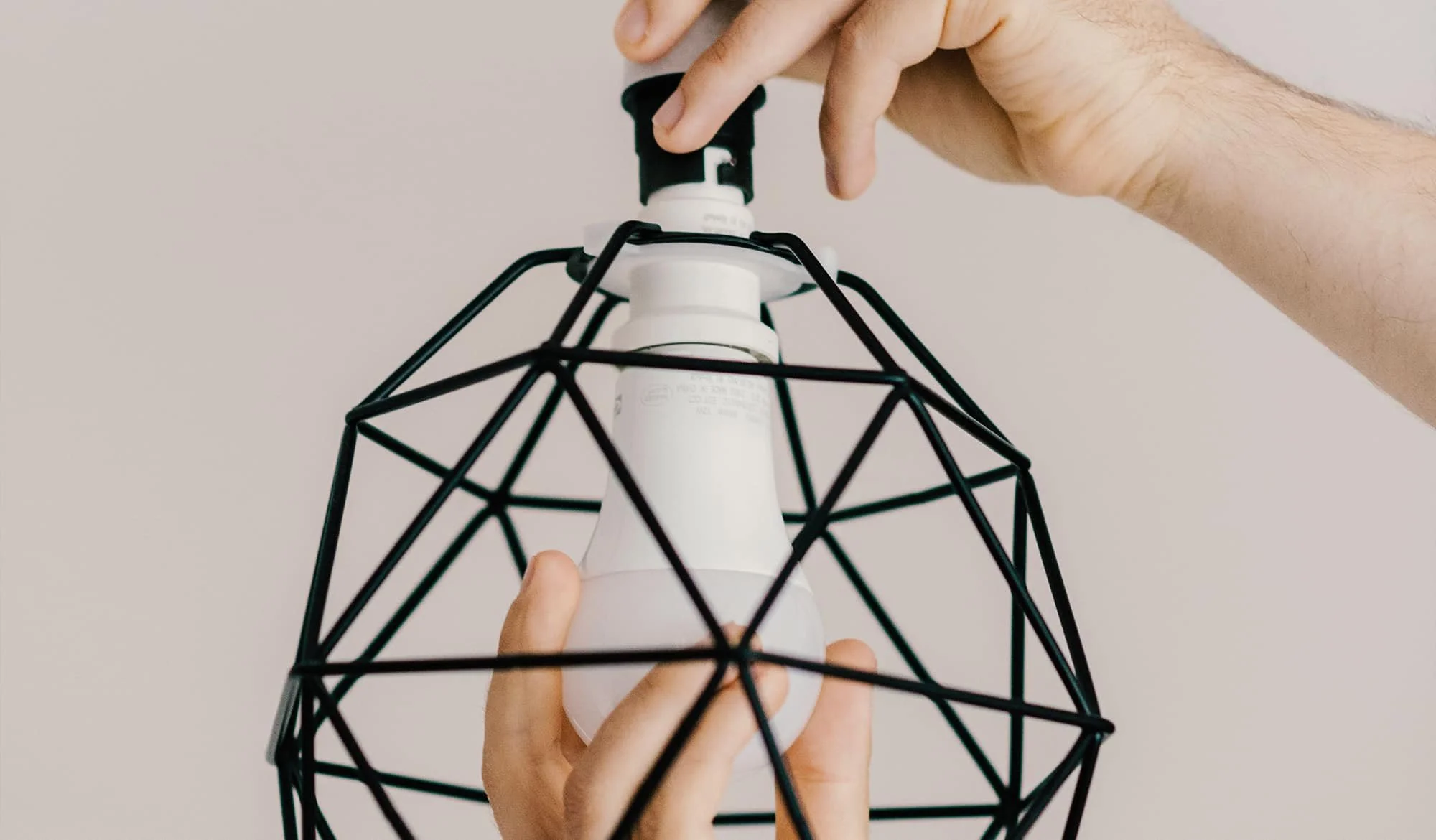 Person inserting a light bulb into a black wire geometric lampshade.