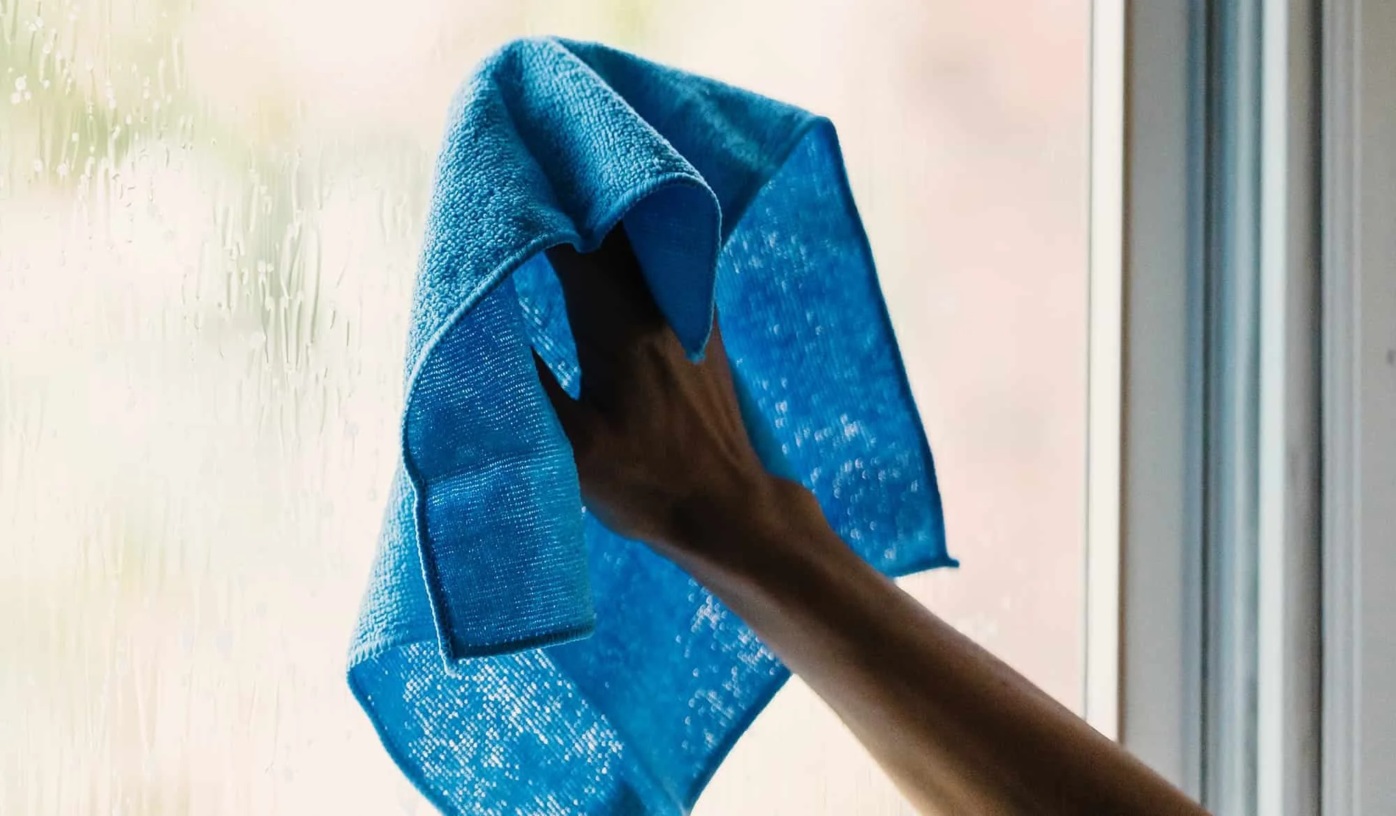 Person cleaning glass window with a blue microfiber cloth.