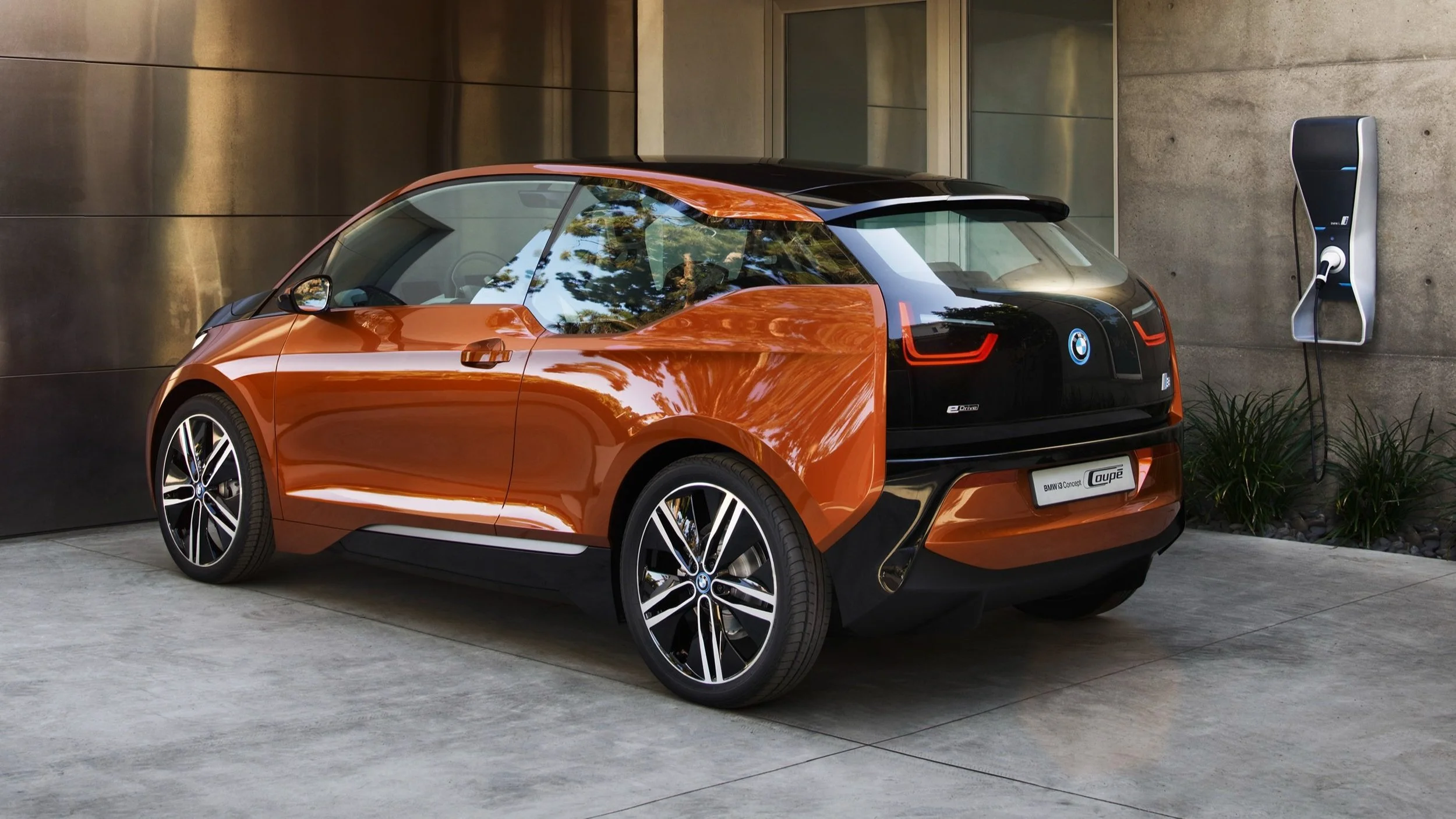 Ein orange-schwarzer BMW i3 Elektrowagen, der an einer Ladestation aufgeladen wird.